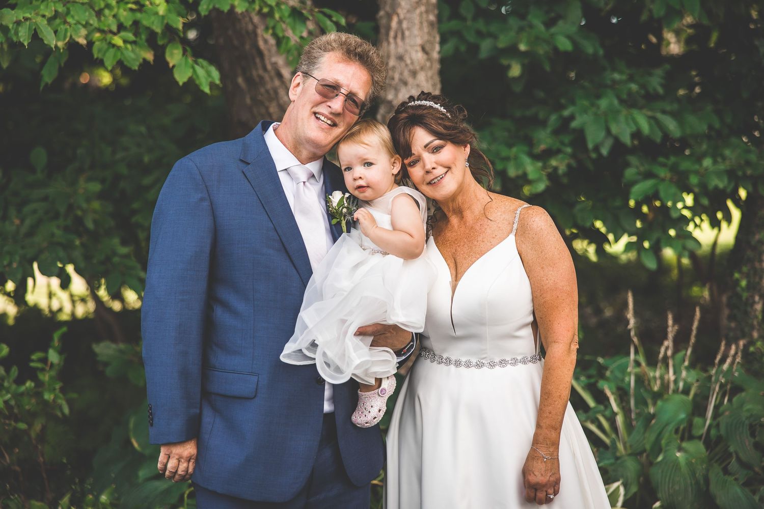 Wedding ceremony taking place outdoors in a lush garden setting with greenery and trees in the background.