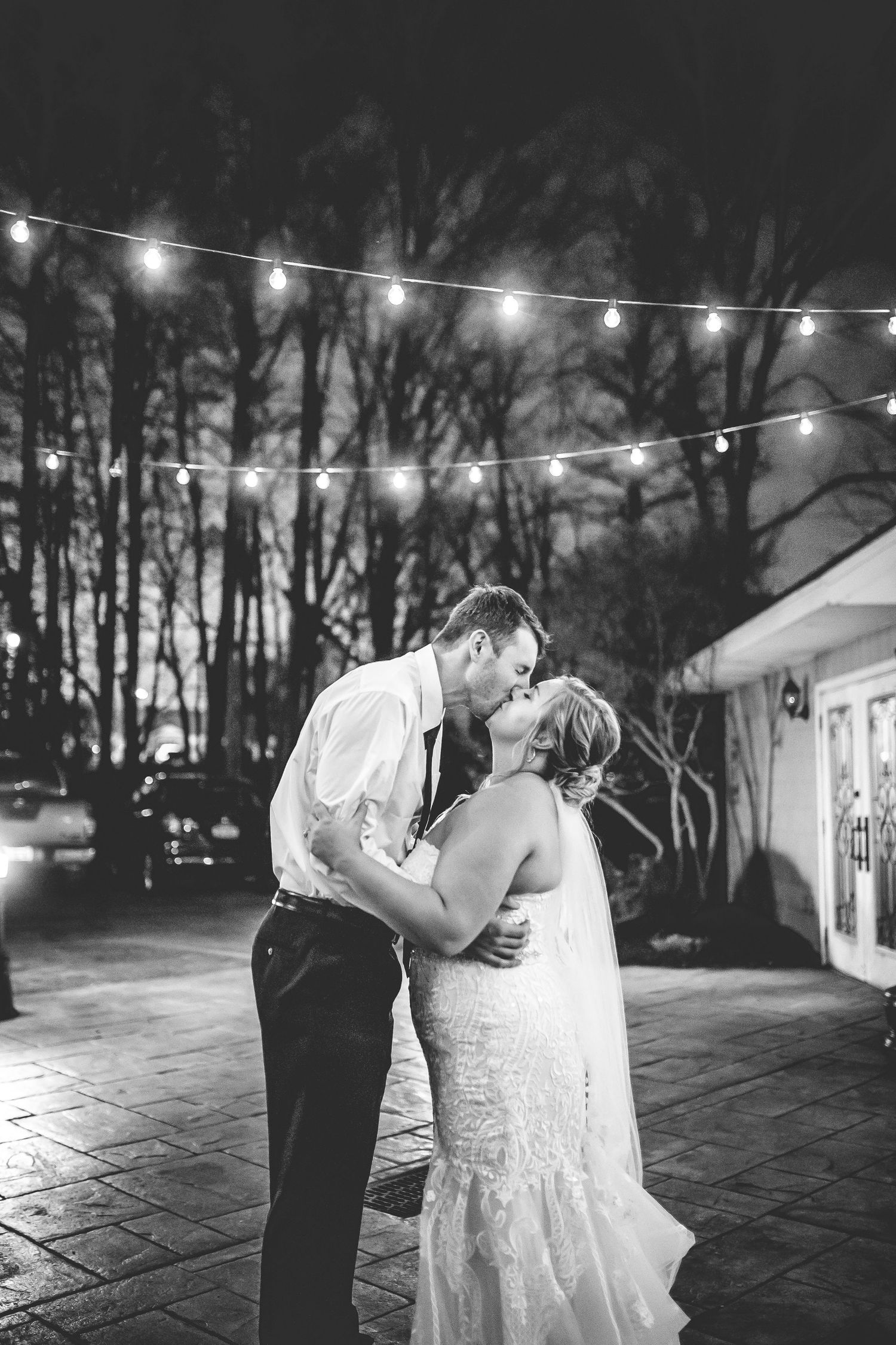 A couple shares a romantic dance under string lights during an evening outdoor reception.
