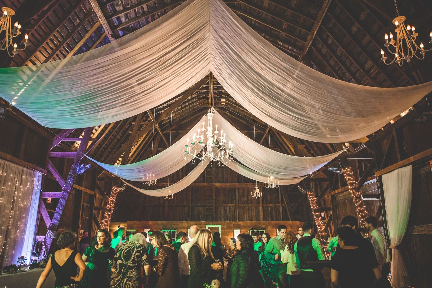 White fabric draping and colorful lighting create an elegant ceiling treatment at a wedding reception.