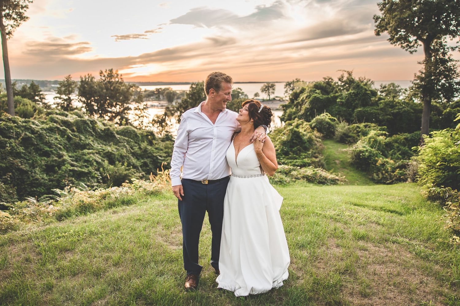 Wedding couple embracing on a grassy hilltop during golden hour.