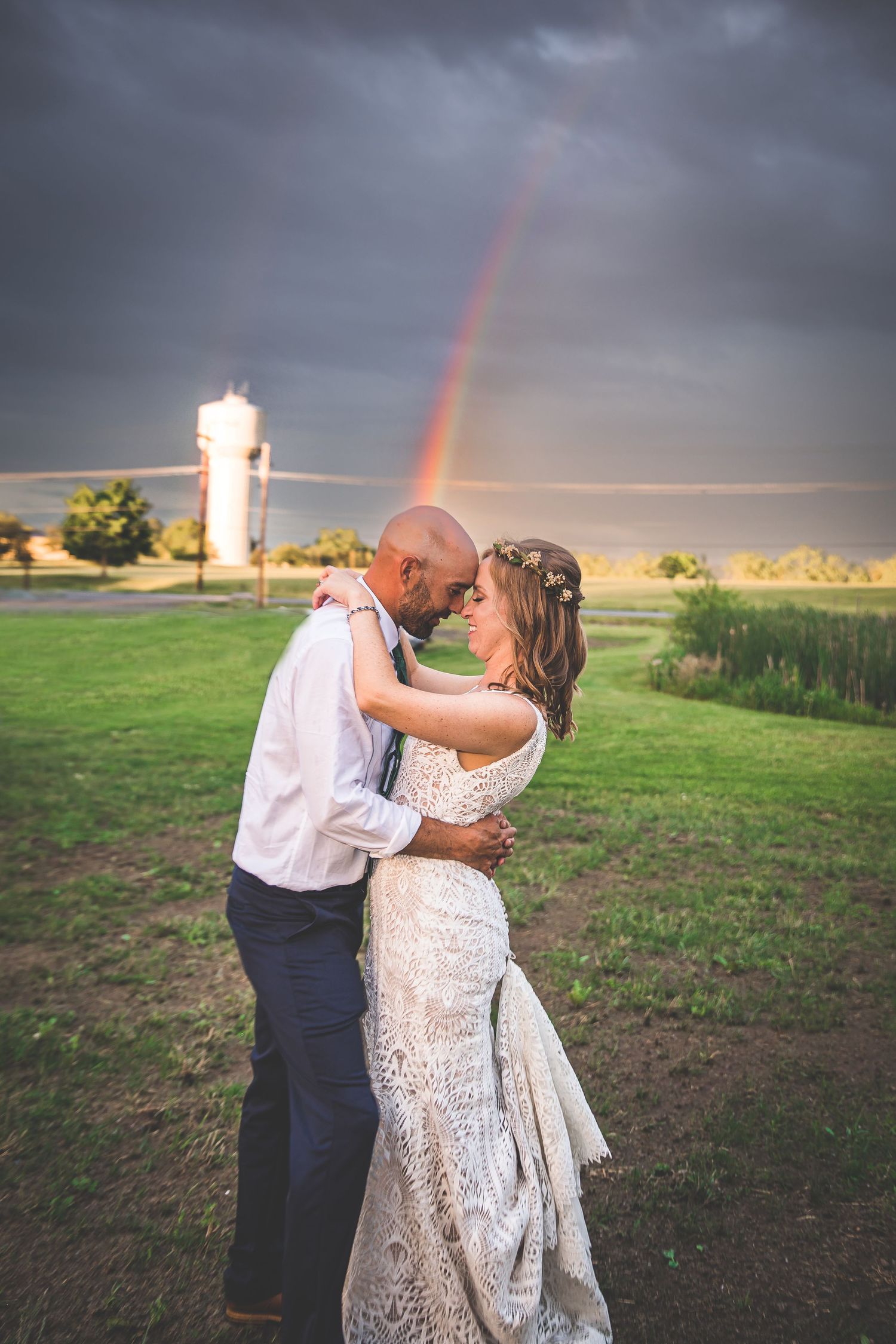 A couple dances in a field at sunset with a dramatic rainbow in the stormy sky.