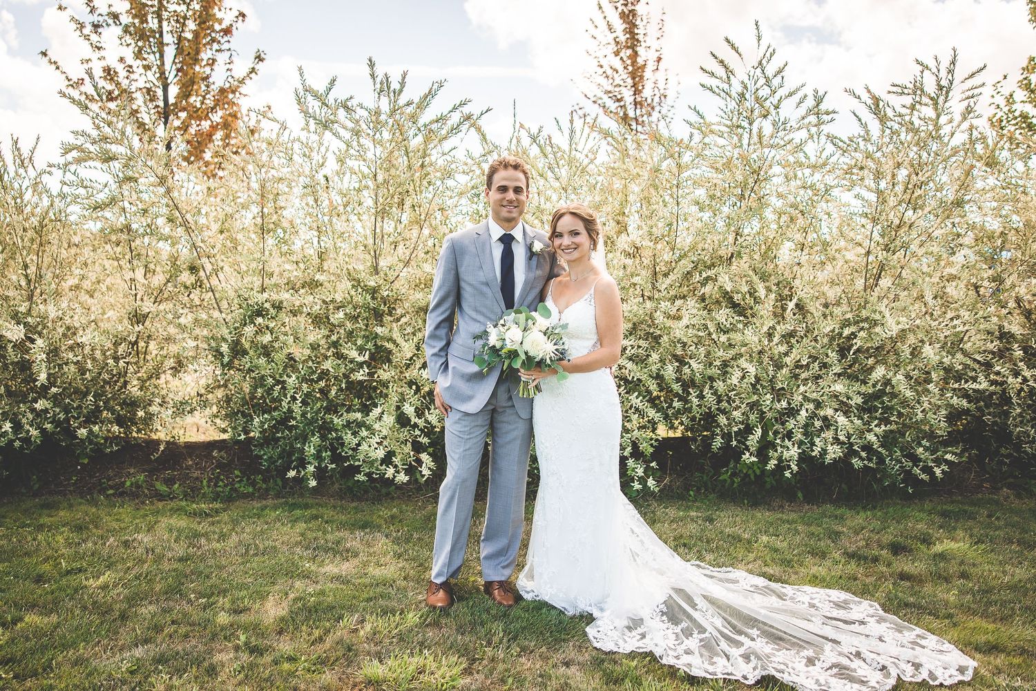 Wedding couple poses against backdrop of flowering trees in spring garden.