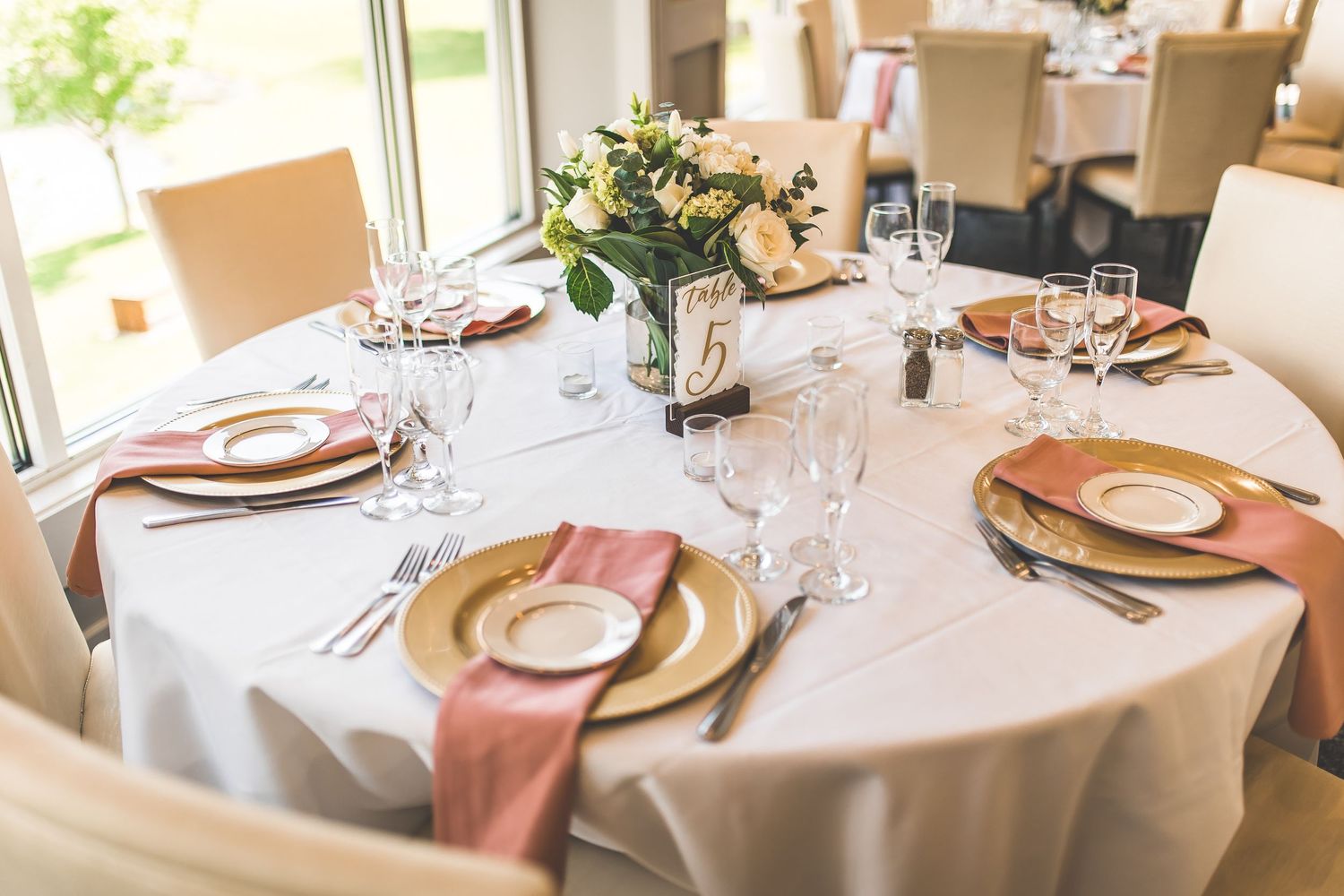 Wedding reception table settings with gold chargers and rose gold accents.