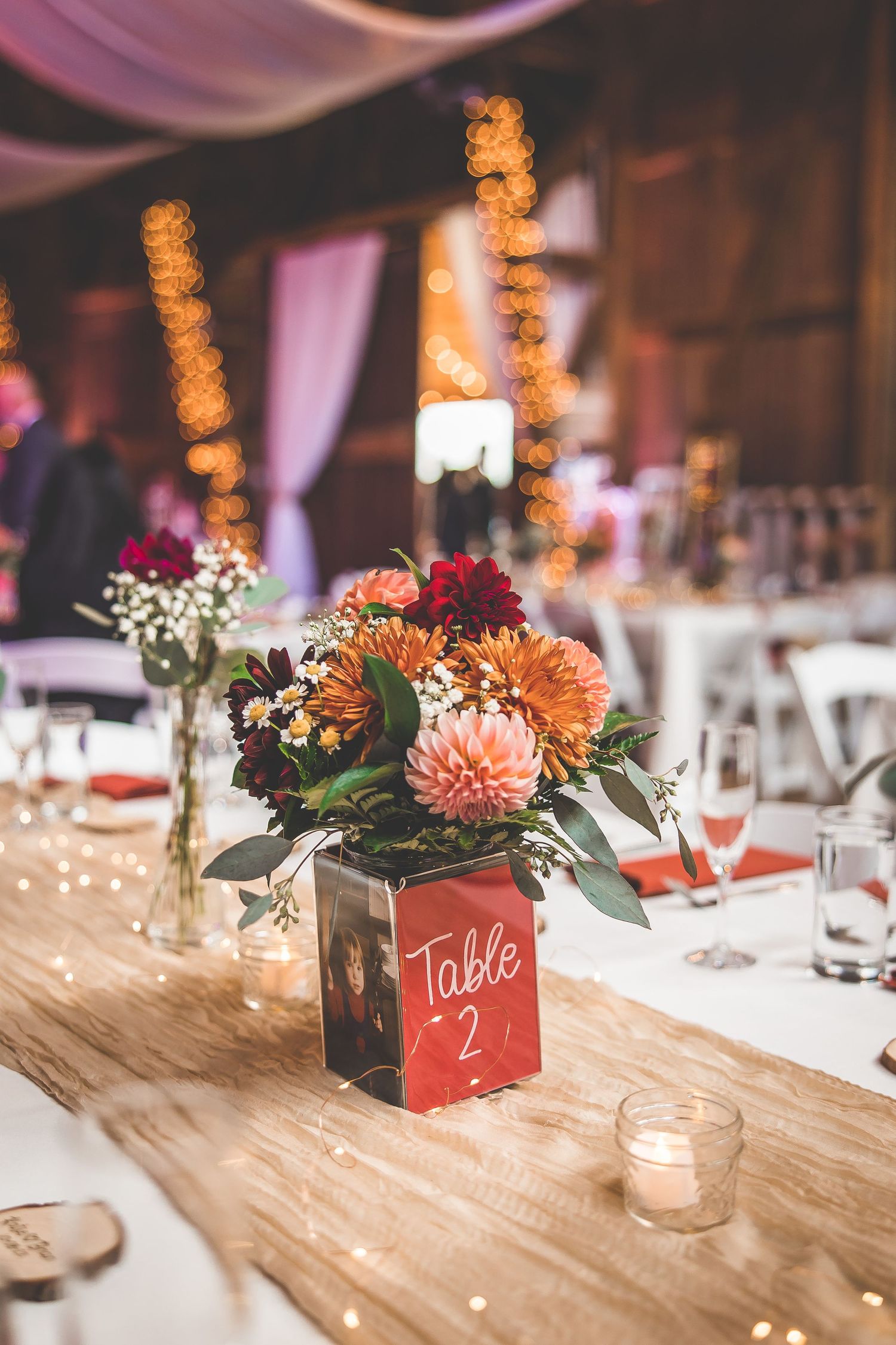 Rustic wedding reception table decor with orange dahlias and table numbers in wooden boxes.