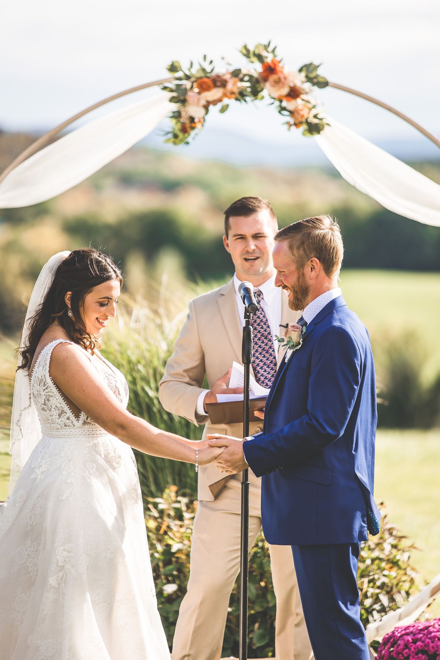 Wedding ceremony under a floral-decorated arch with white fabric draping and mountains in the background.