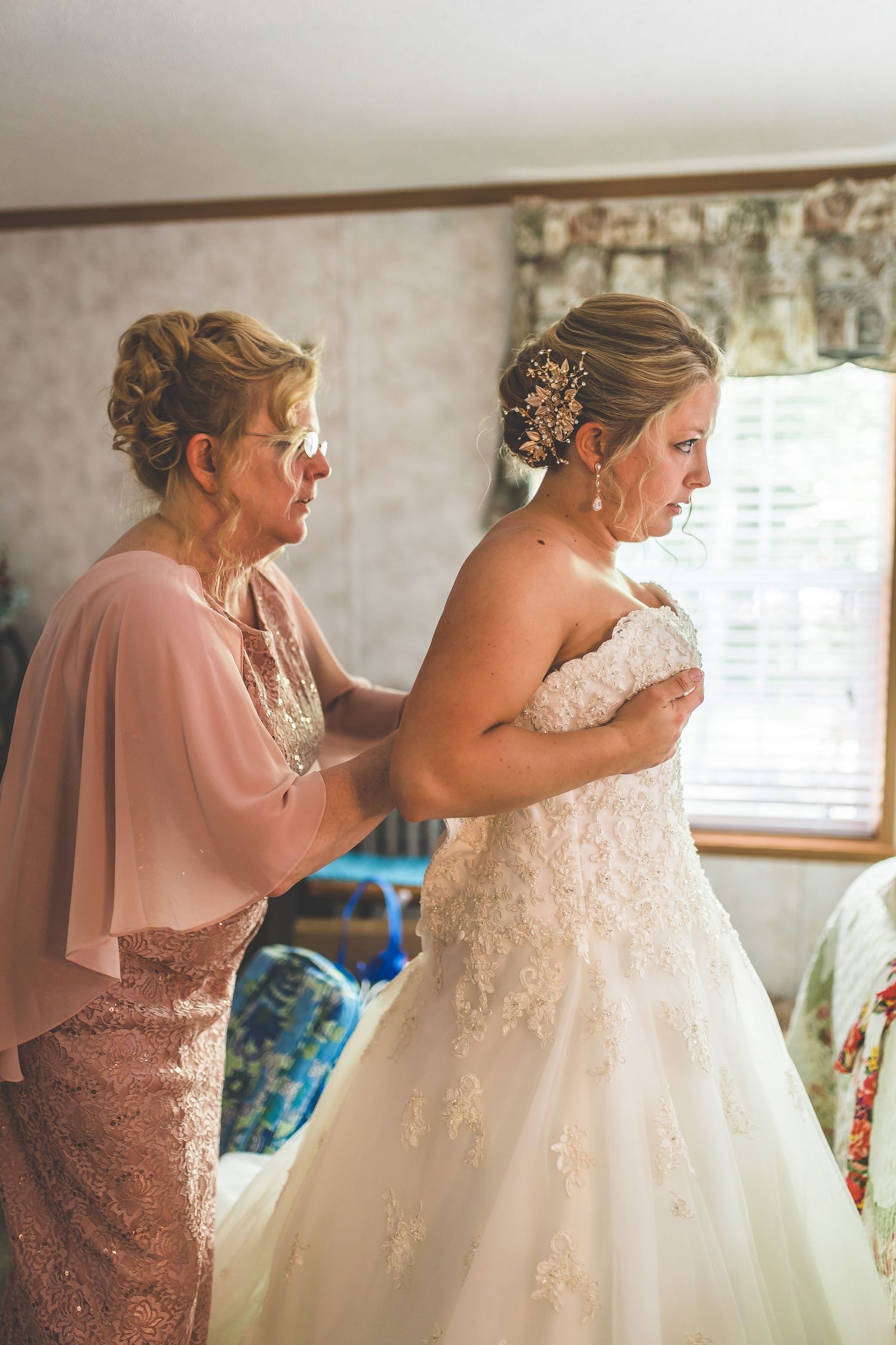 Intimate moment of wedding dress preparation in sunlit room.