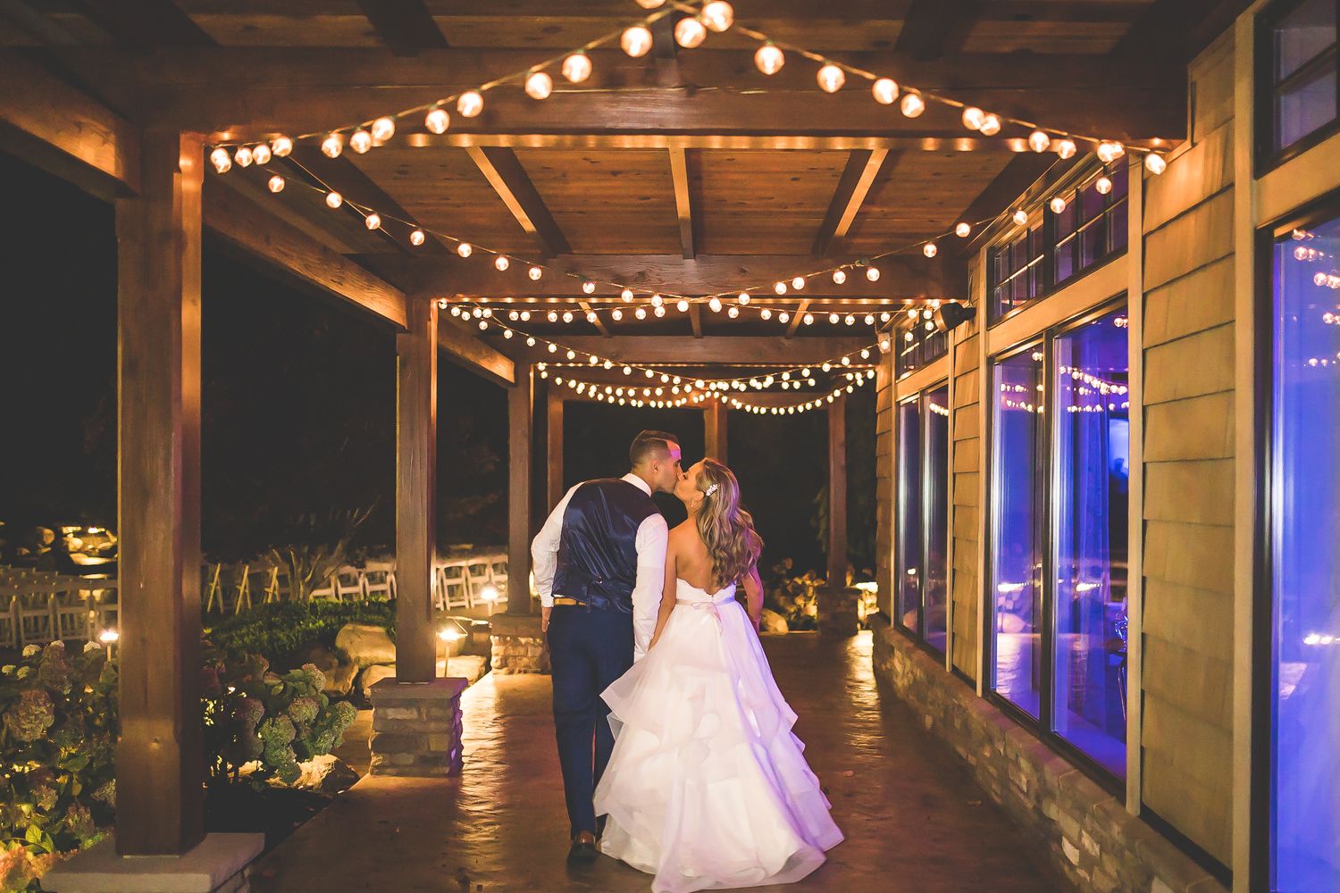 String lights illuminate a rustic wooden venue hallway creating a romantic wedding reception atmosphere.