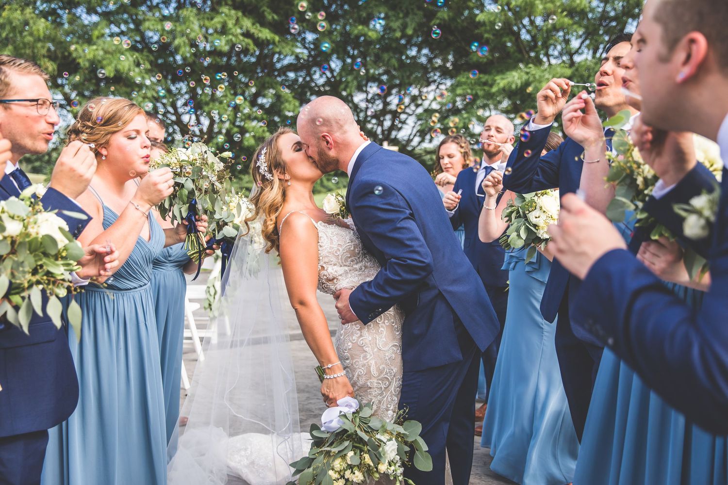 Wedding party in navy and light blue attire celebrates outdoors on a sunny day.