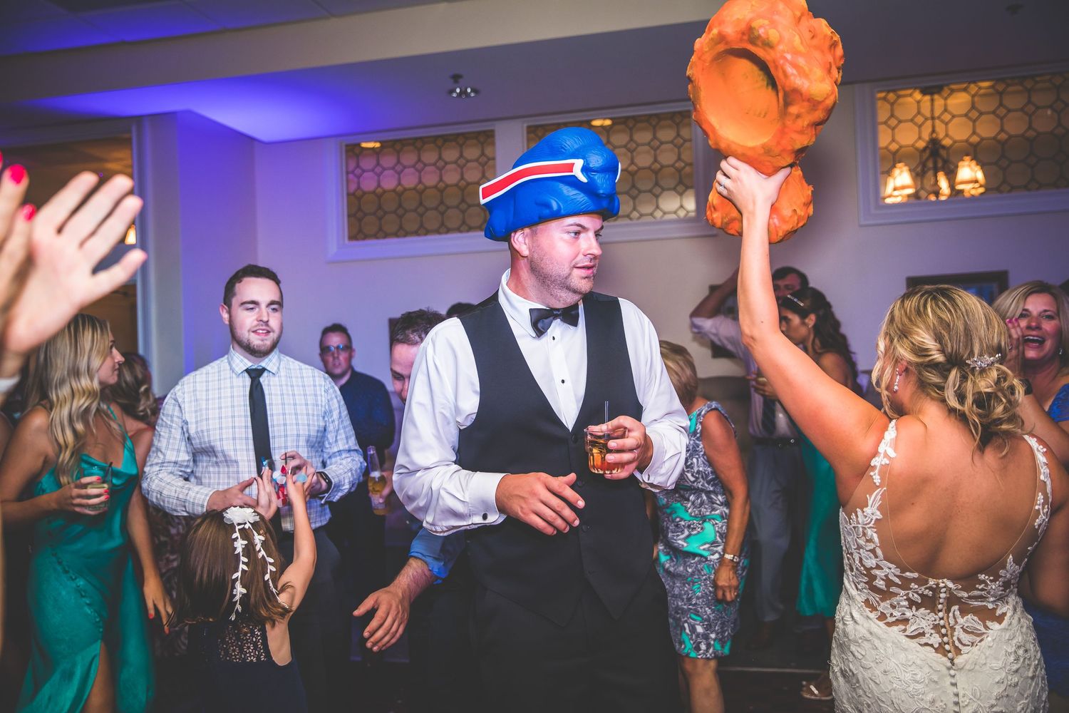 Party guests dancing and celebrating with colorful props and festive attire at a wedding reception.