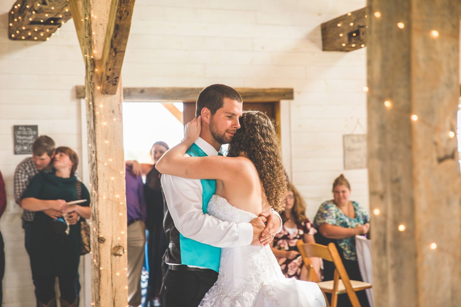 A couple shares their first dance at a rustic barn wedding reception with string lights overhead.