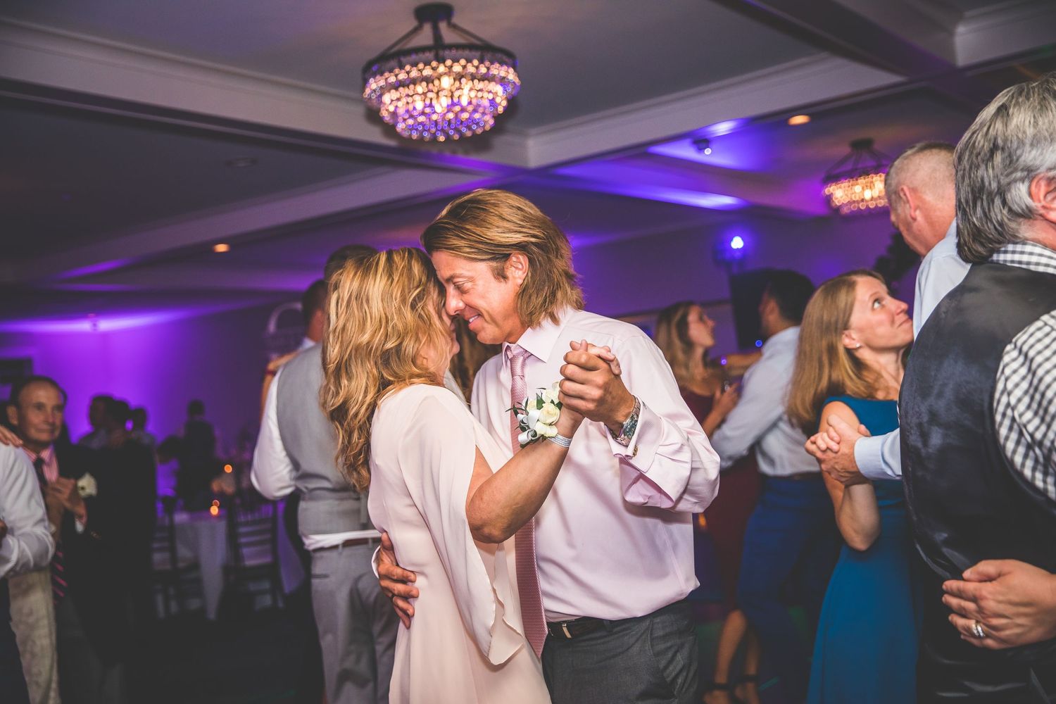 Wedding guests enjoying themselves on a dance floor illuminated by purple ambient lighting.