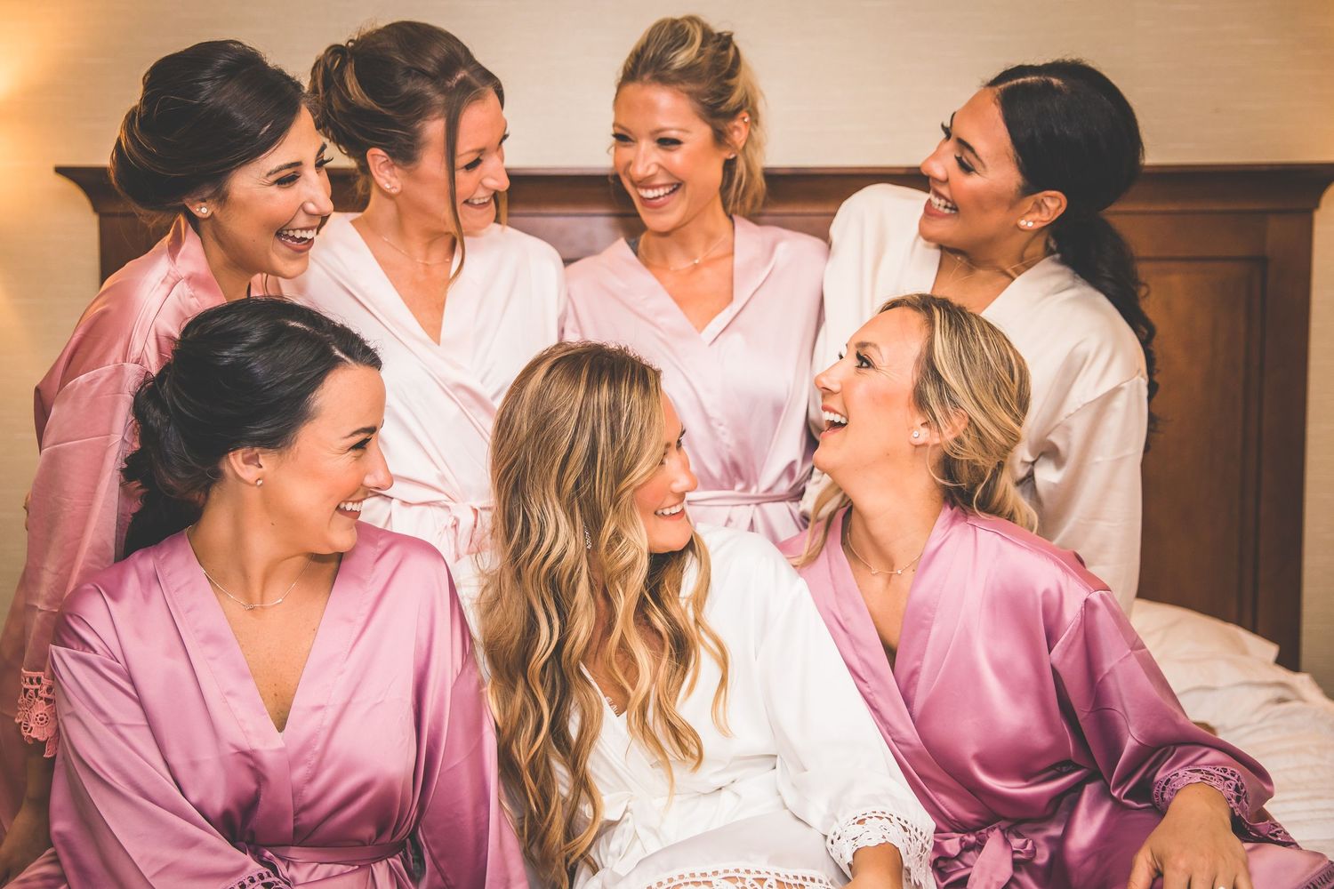 Group of women in pink satin robes share joyful moments while getting ready.