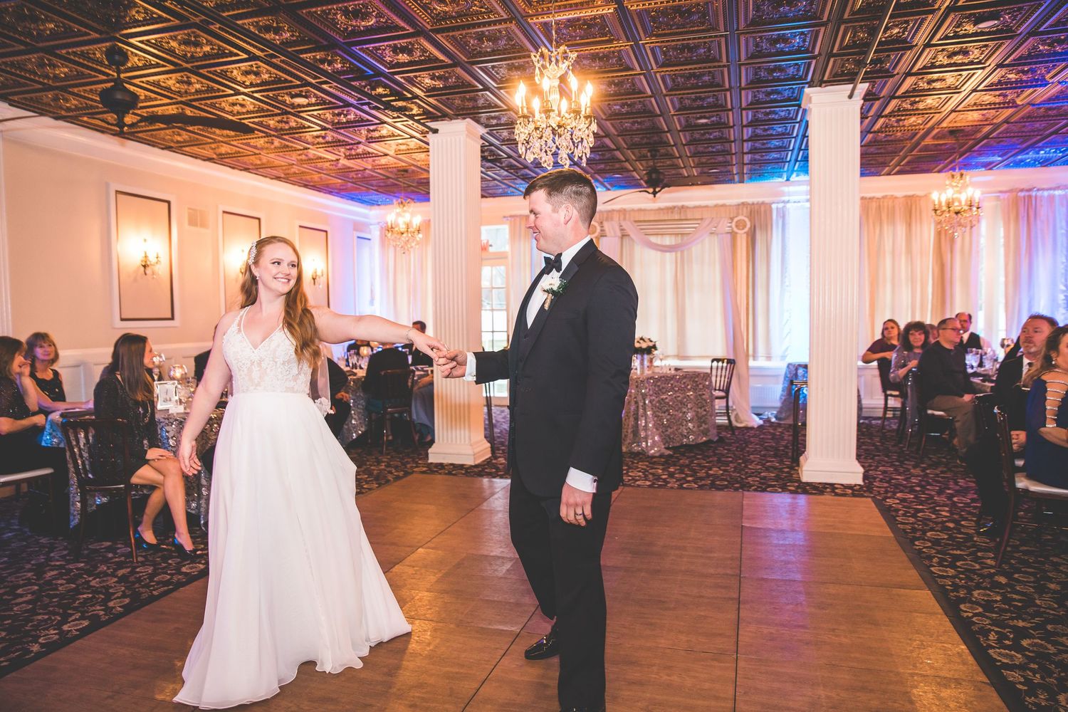 Wedding couple dancing in an elegant ballroom with purple lighting and ornate ceiling details.