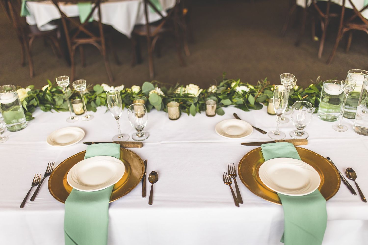 Wedding reception table with mint napkins, gold chargers, and fresh greenery centerpiece runner.