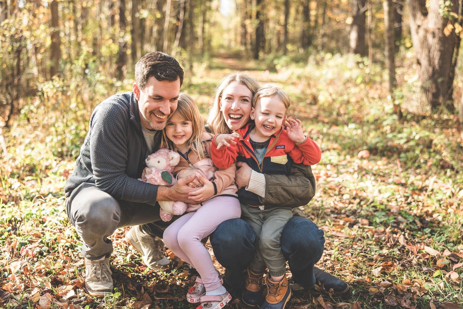 Family enjoying autumn day together in a sunlit forest with golden leaves.