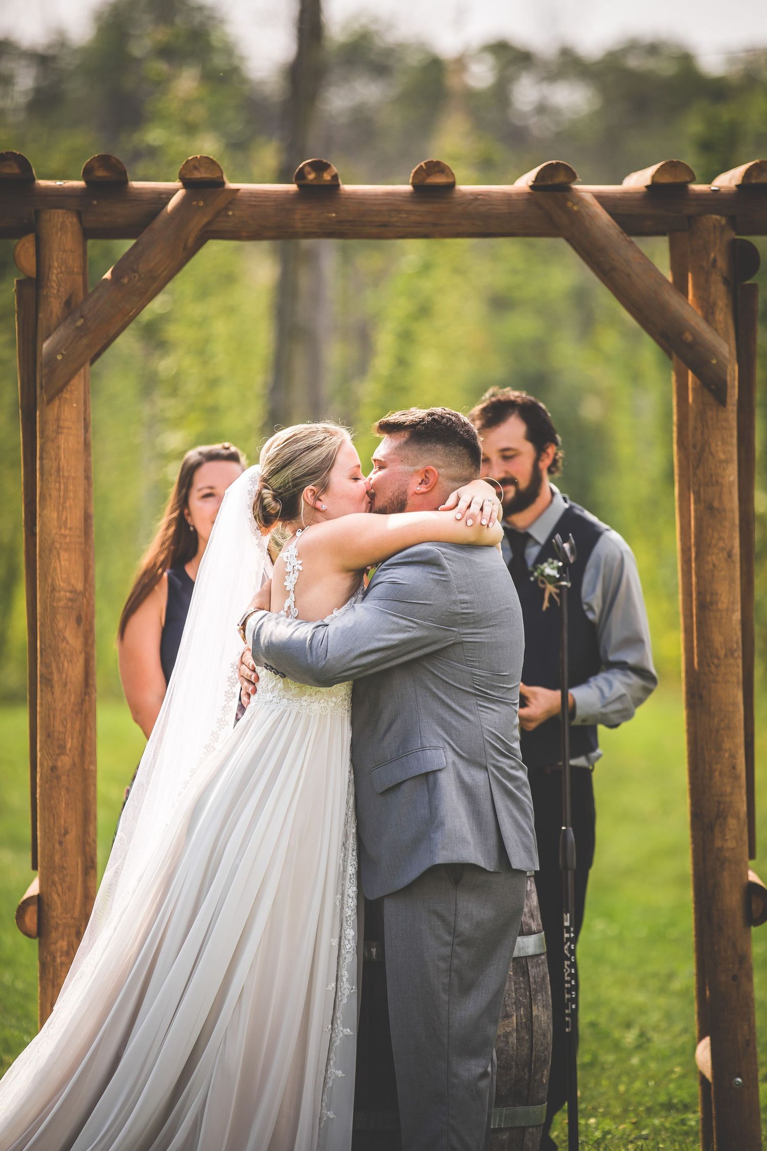Wedding ceremony celebration under wooden pergola with guests seated in garden setting.