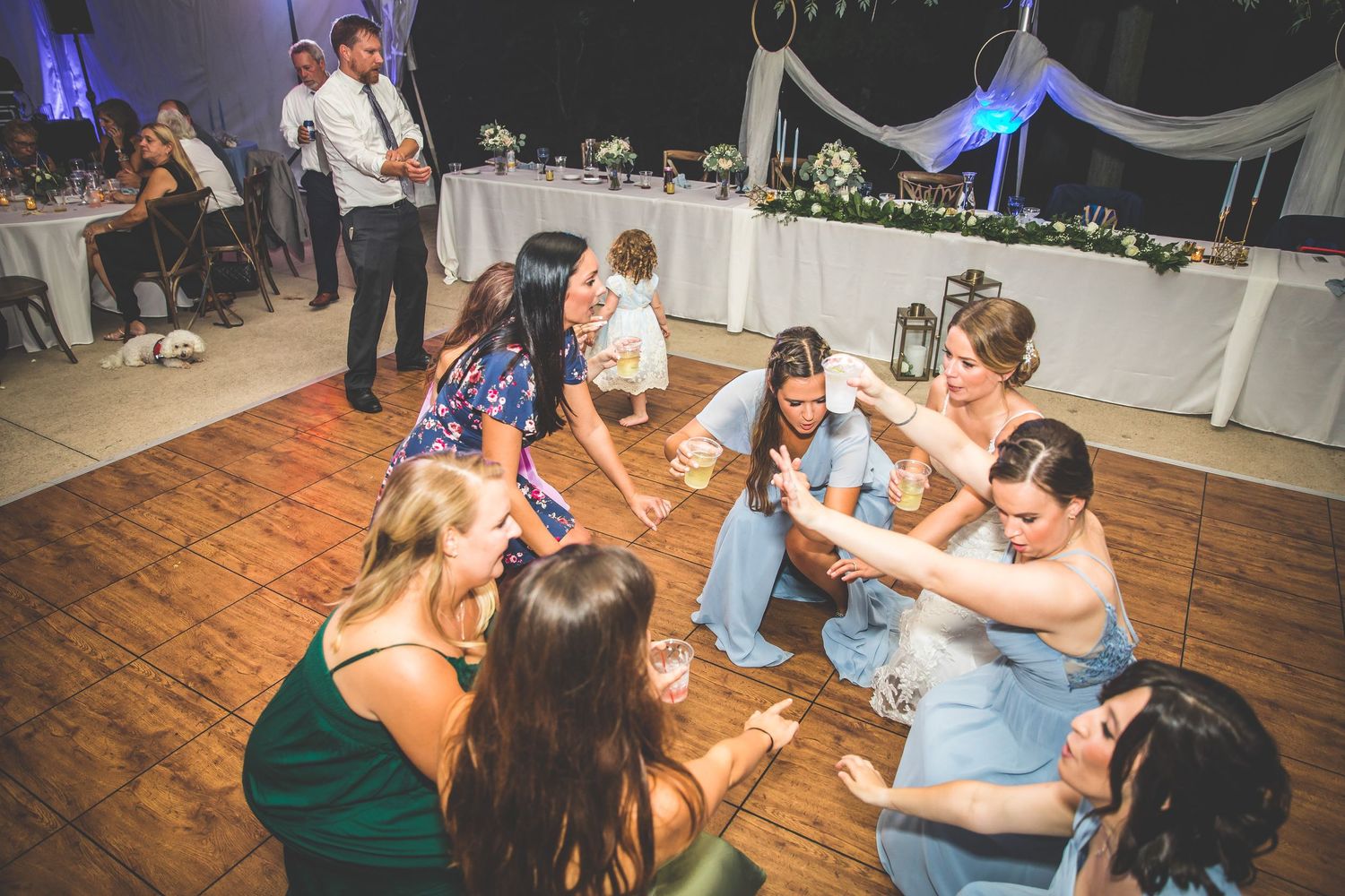 Wedding guests dancing and celebrating on a wooden dance floor under tent lighting.