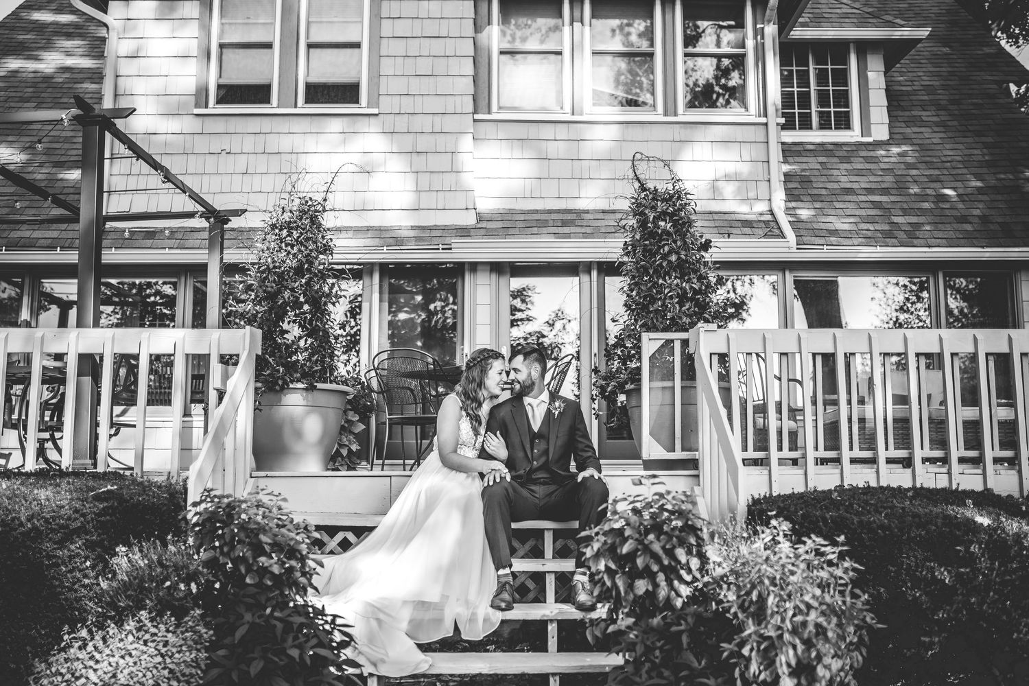 Black and white portrait of couple on steps of classic shingle-style house.