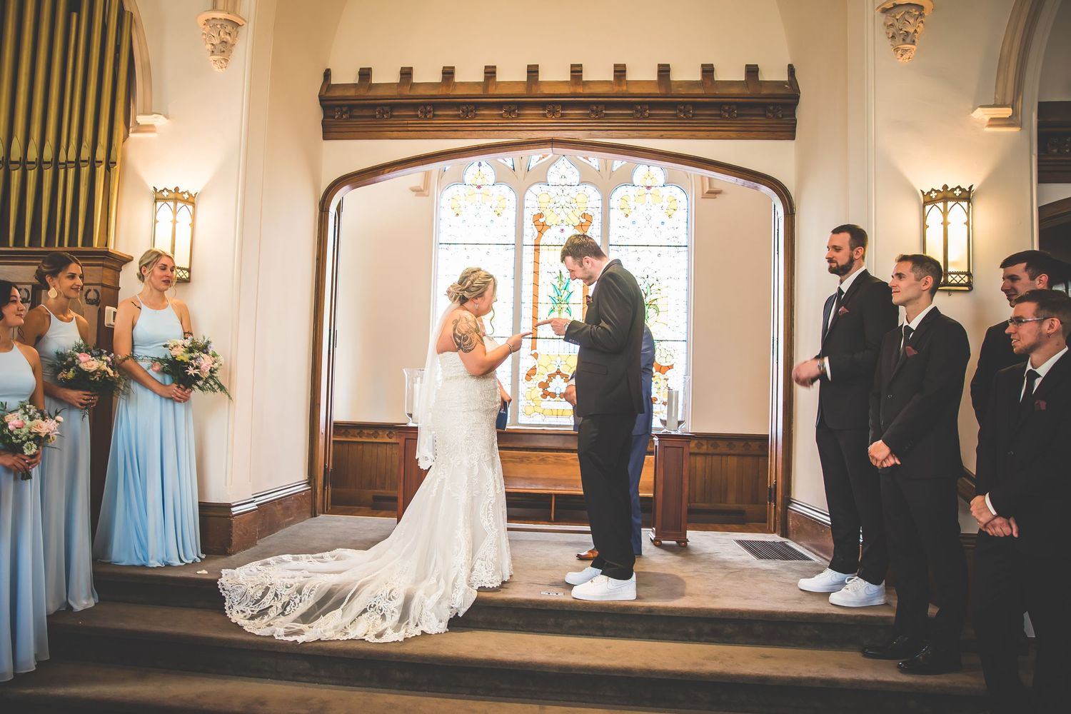 Romantic first kiss between newlyweds in a church sanctuary with beautiful stained glass windows and wooden details.