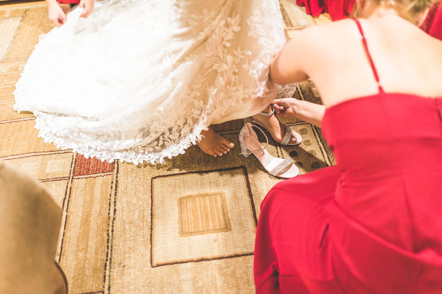 Close-up details of wedding dress preparations with red bridesmaid dresses in the background.
