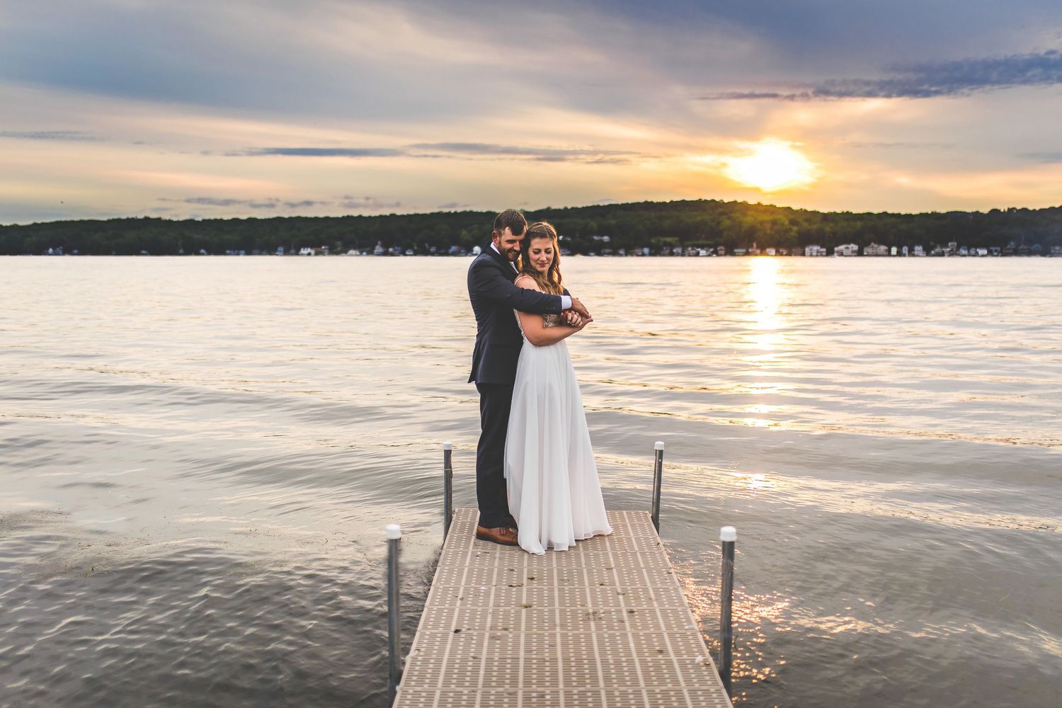 Romantic sunset wedding photos on a lakeside dock with water and sky views.