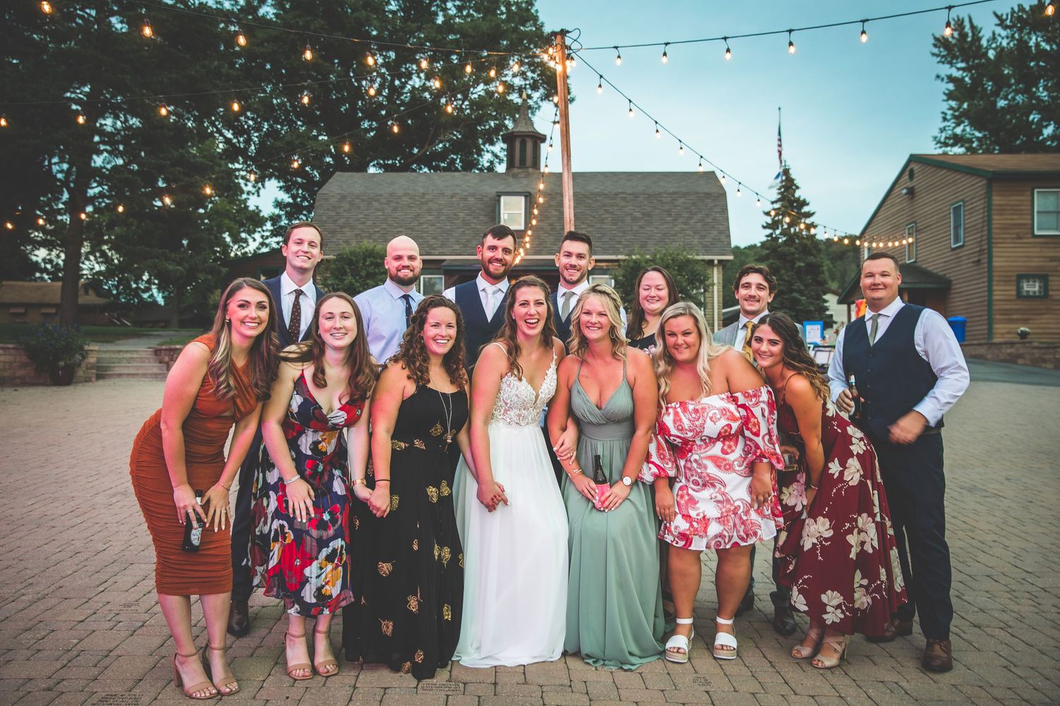 Wedding party guests gather outdoors under string lights during a summer celebration.