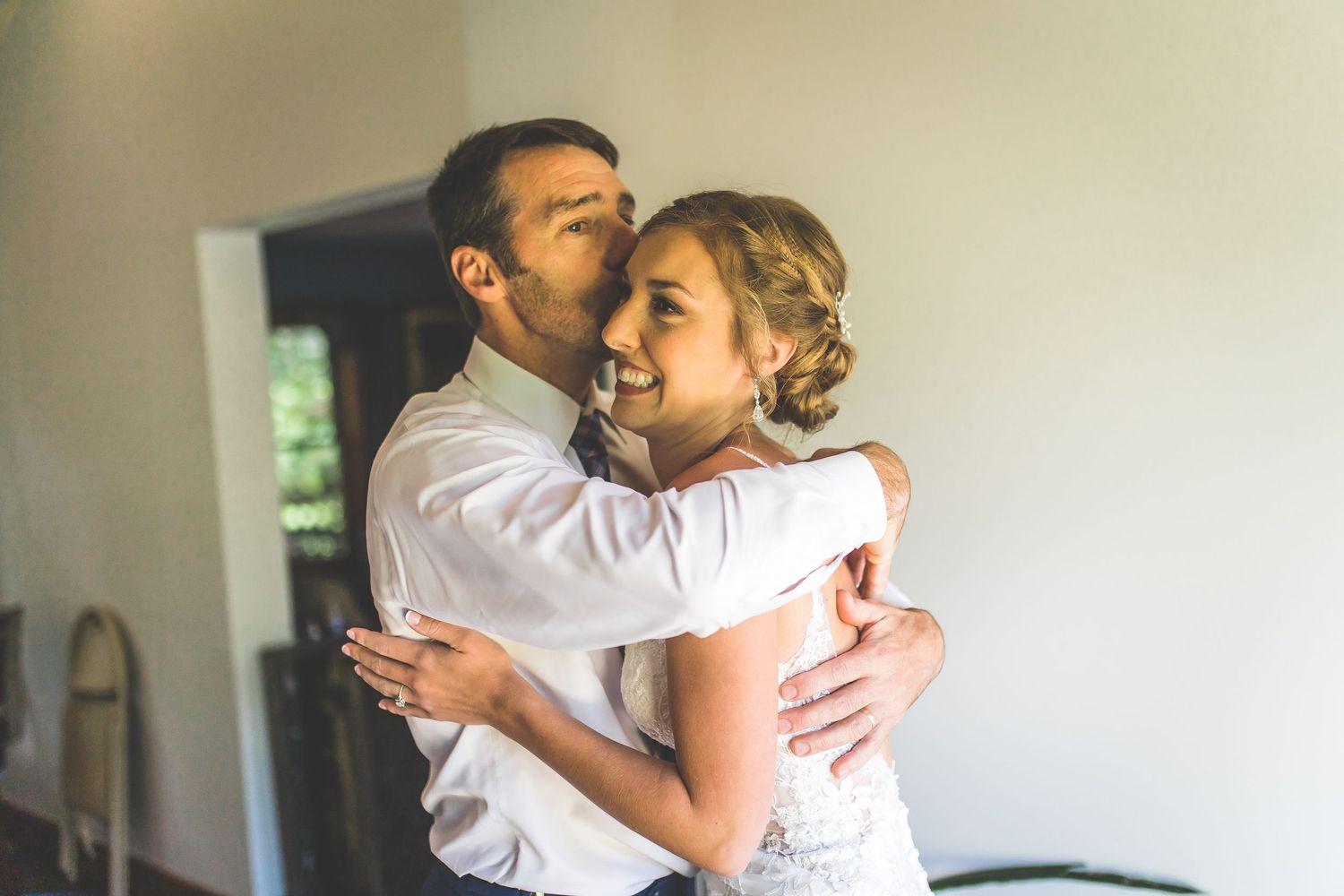 Emotional first look moment between couple embracing in sunlit indoor setting.
