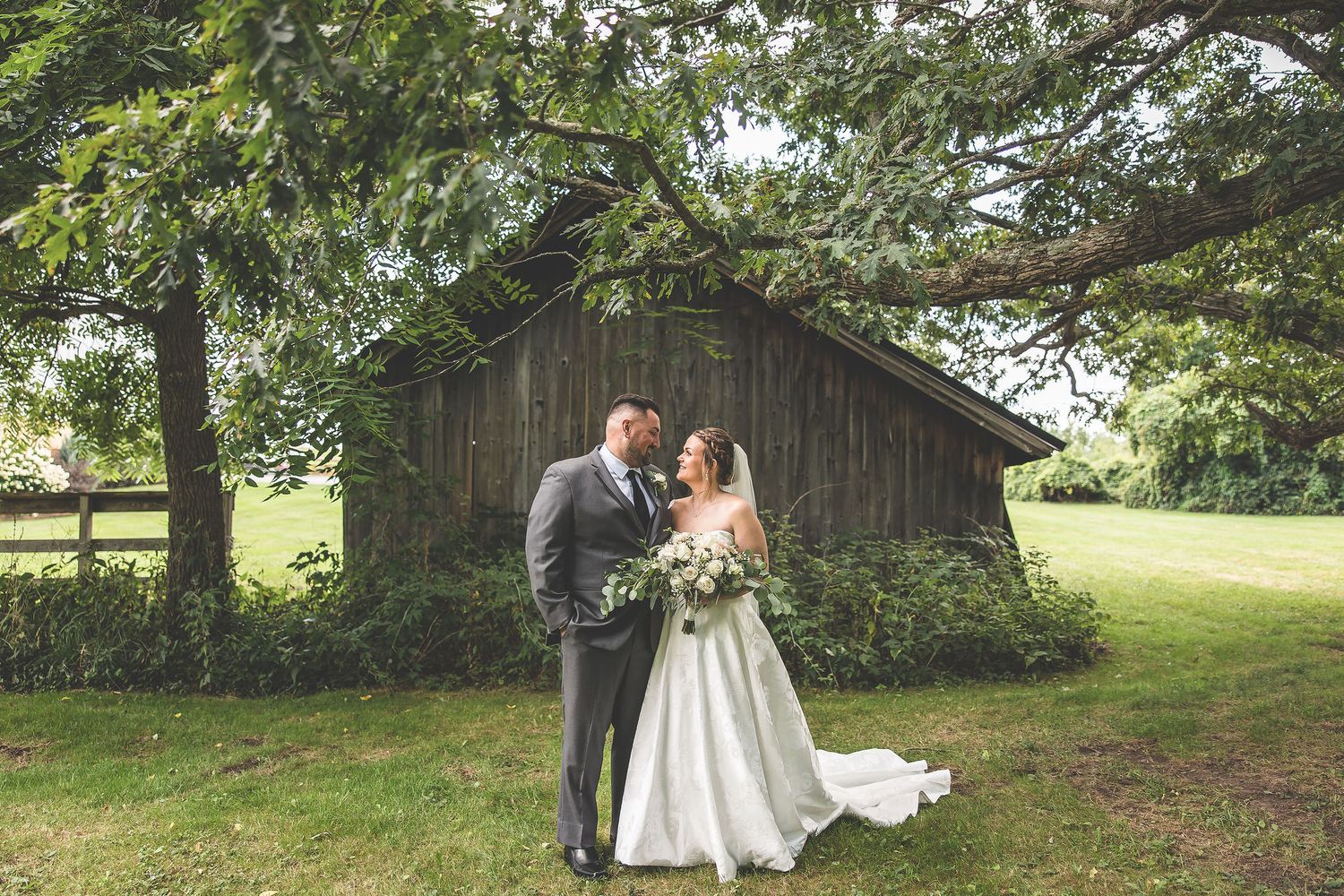 Wedding couple poses for romantic photos in a scenic outdoor setting with a rustic barn backdrop.