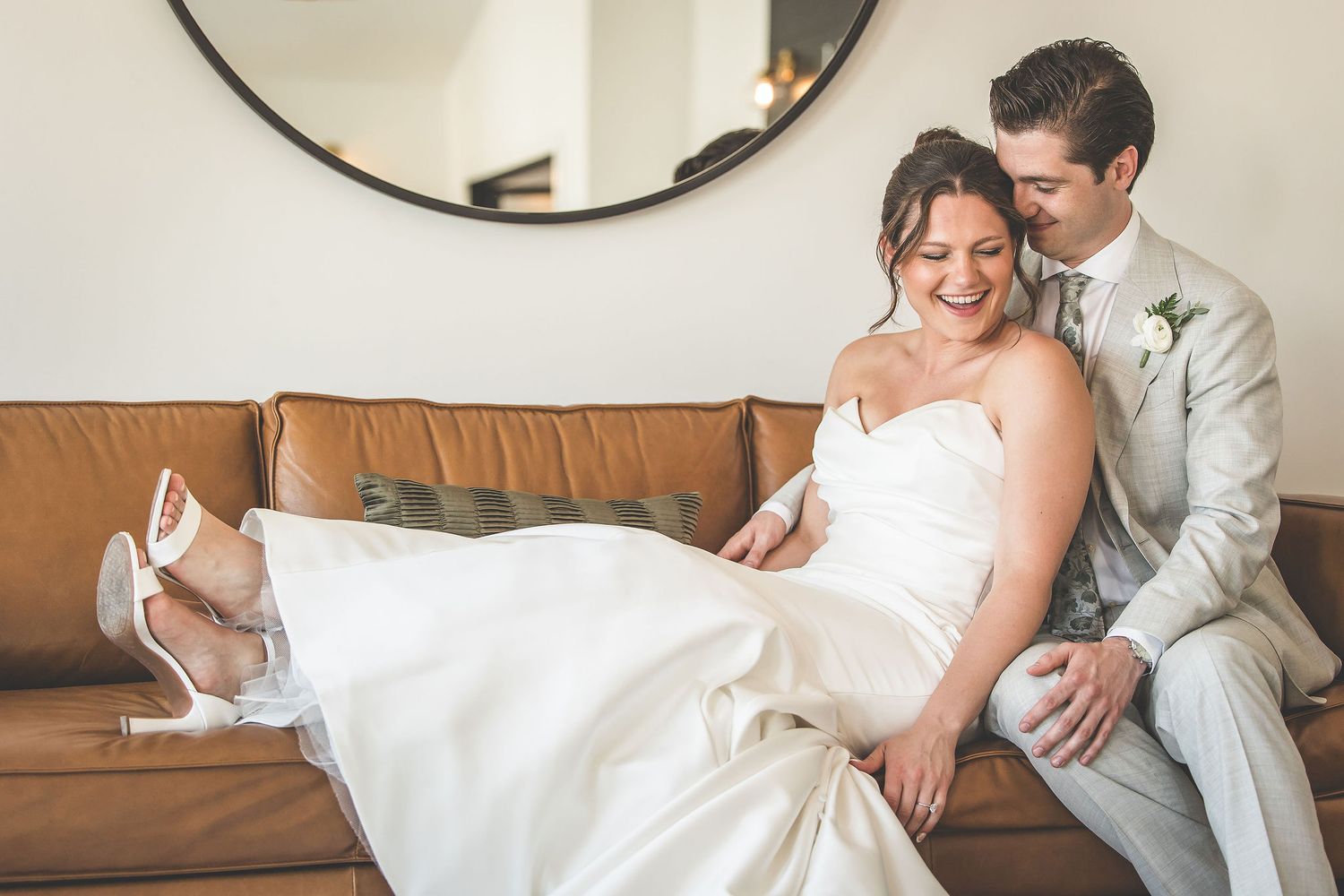 Wedding couple sharing intimate moments on a brown leather couch in a bright, modern setting.