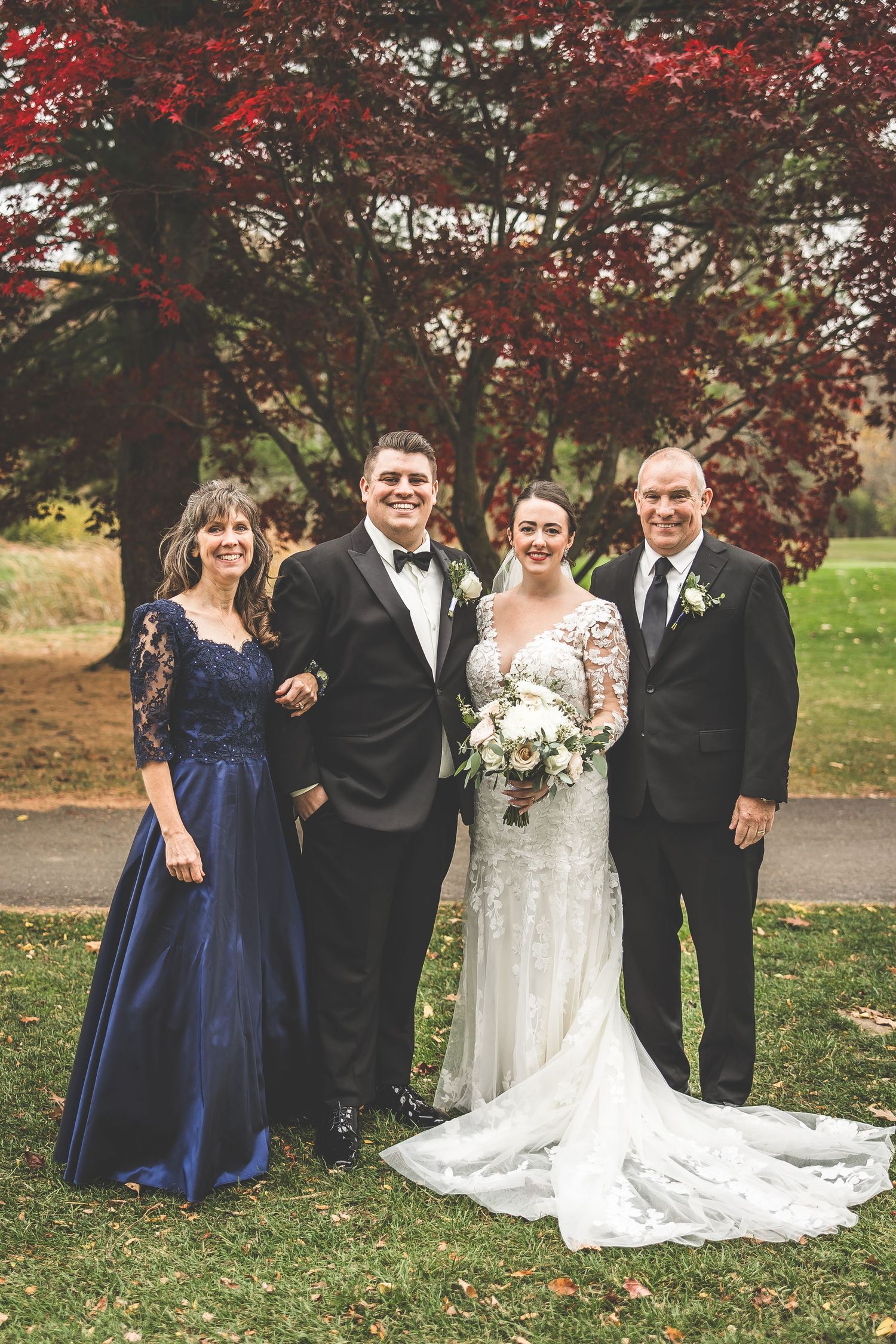 Wedding party in navy and black attire poses against backdrop of red autumn foliage.