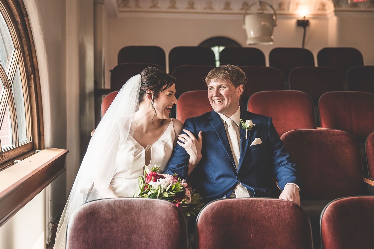 Wedding couple poses among vintage theater seats with dramatic lighting and architectural elements.