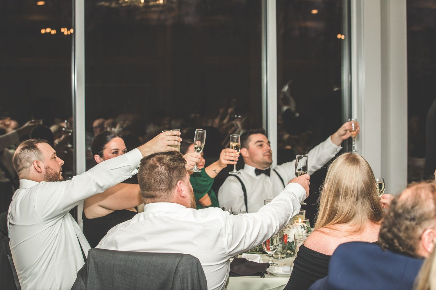 Reception guests raise champagne glasses during wedding toasts in an elegant banquet hall.