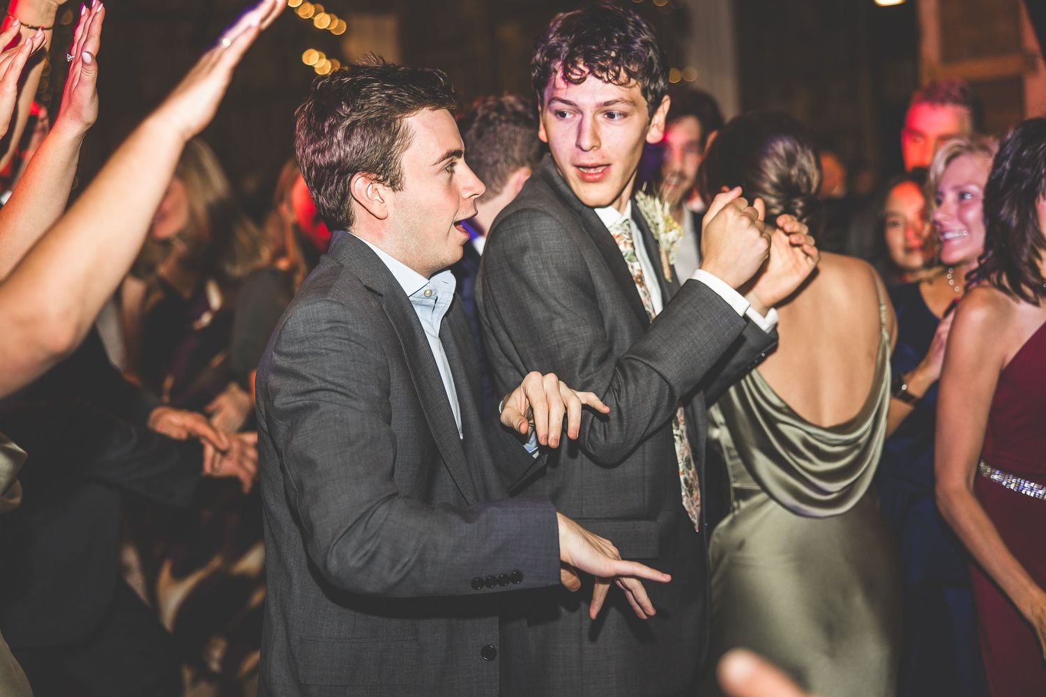 Wedding guests dance and celebrate on a dimly lit dance floor at a rustic barn reception venue.
