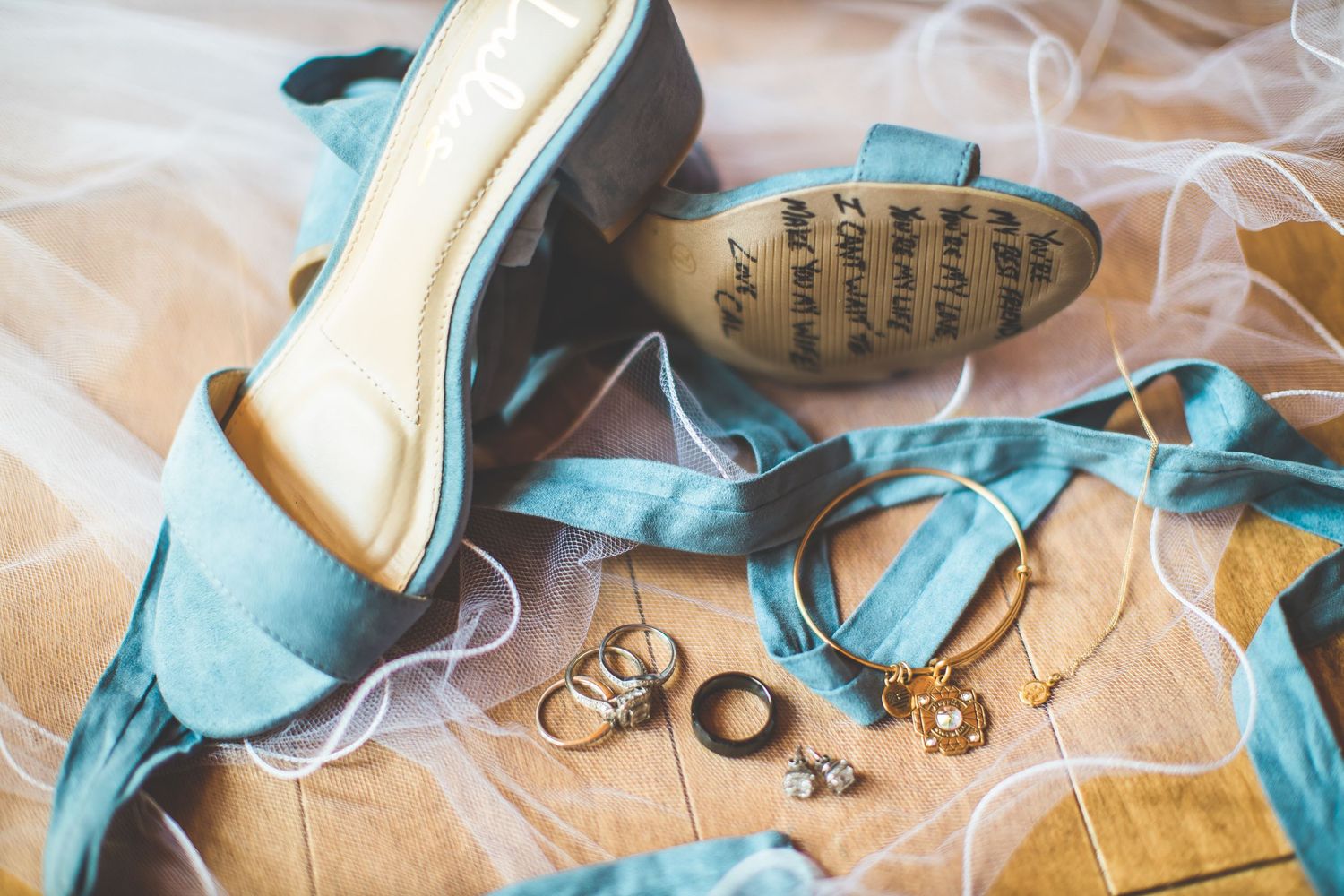 Light blue wedding shoes with ribbons and wedding rings arranged on beige fabric.