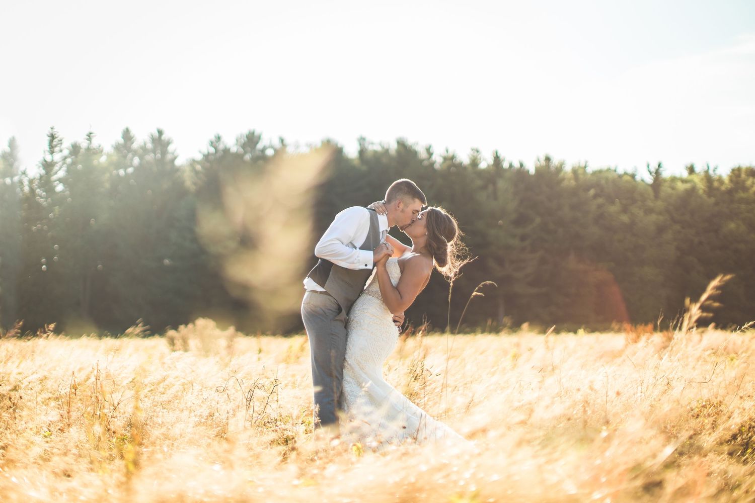 Golden sunset illuminates a grassy field as a couple embraces in an intimate outdoor wedding photoshoot.