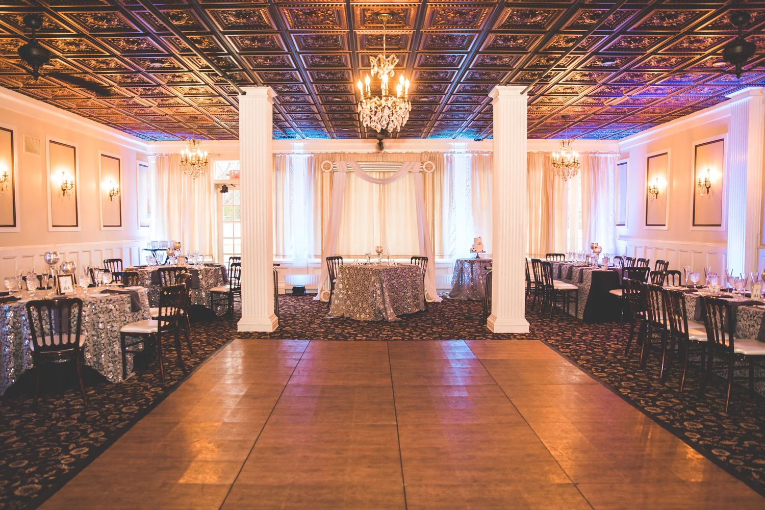Spacious wedding venue with white columns, chandeliers and rows of chairs set for a ceremony.