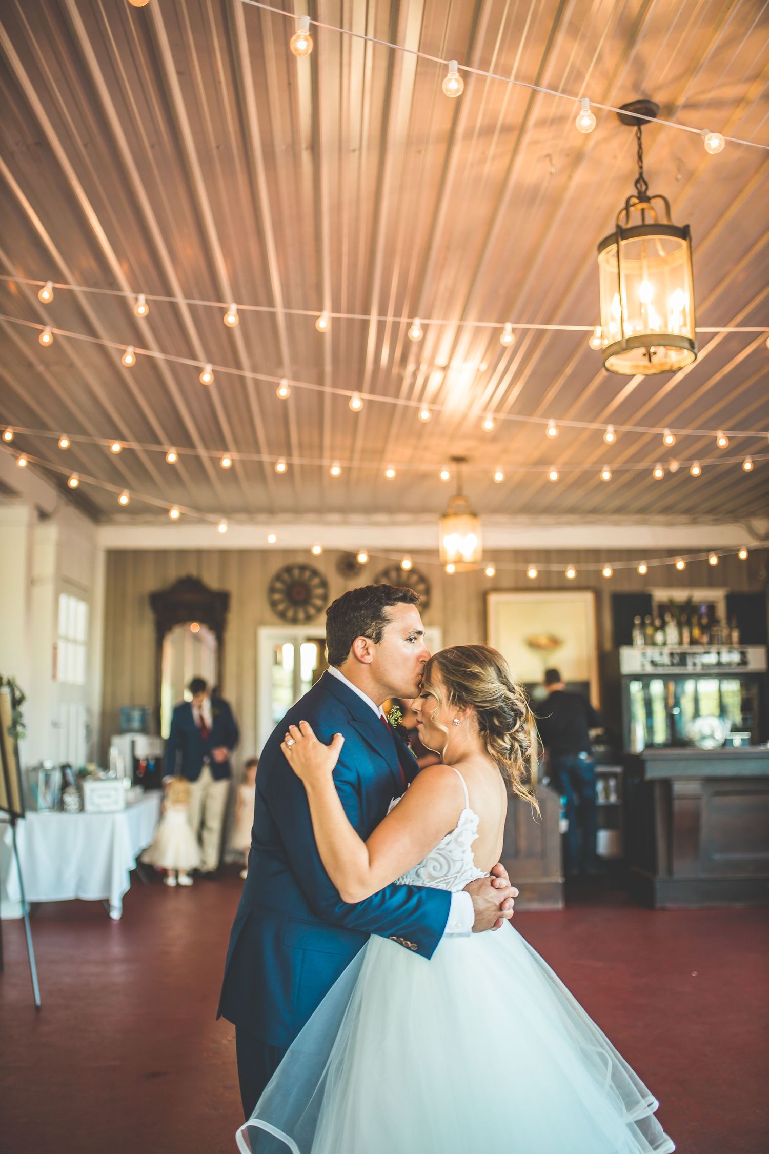 A couple shares their first dance under string lights and chandeliers at their wedding reception.