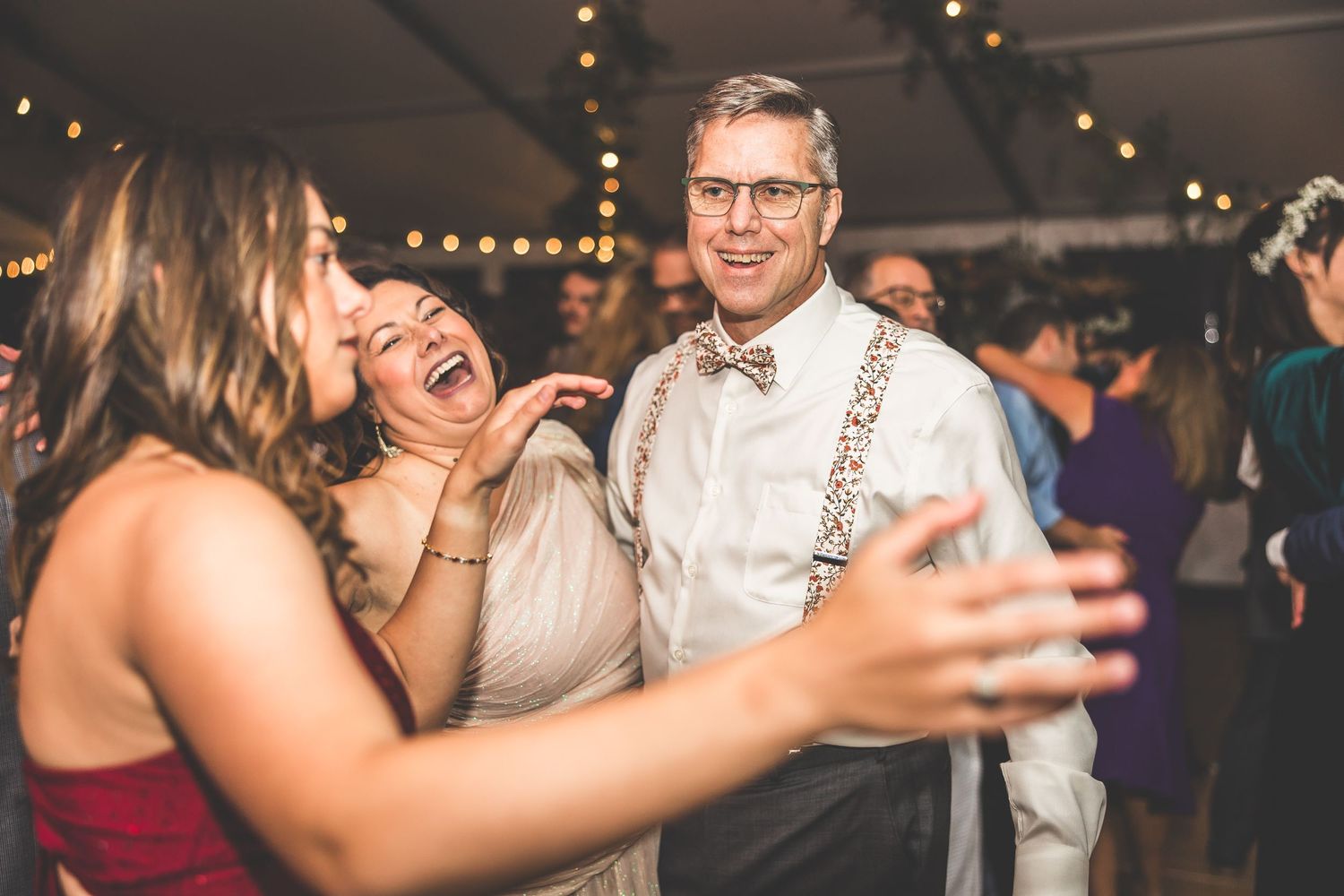 Guests dancing and mingling at a lively wedding reception under string lights.