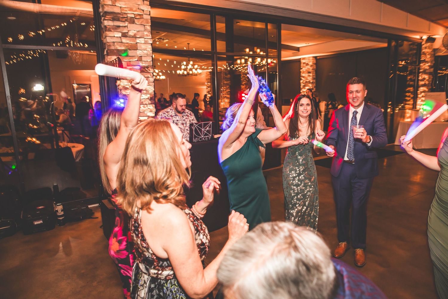 Energetic dance party at wedding reception with string lights and exposed brick walls.