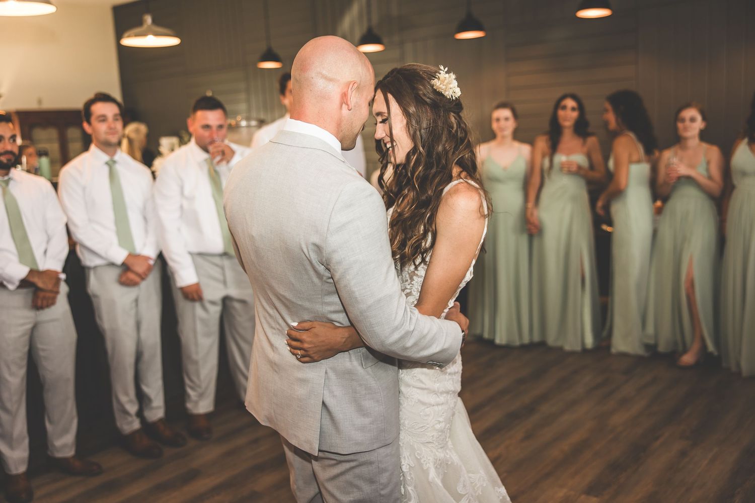 Black and white photo of wedding party dancing in an indoor venue with pendant lights.