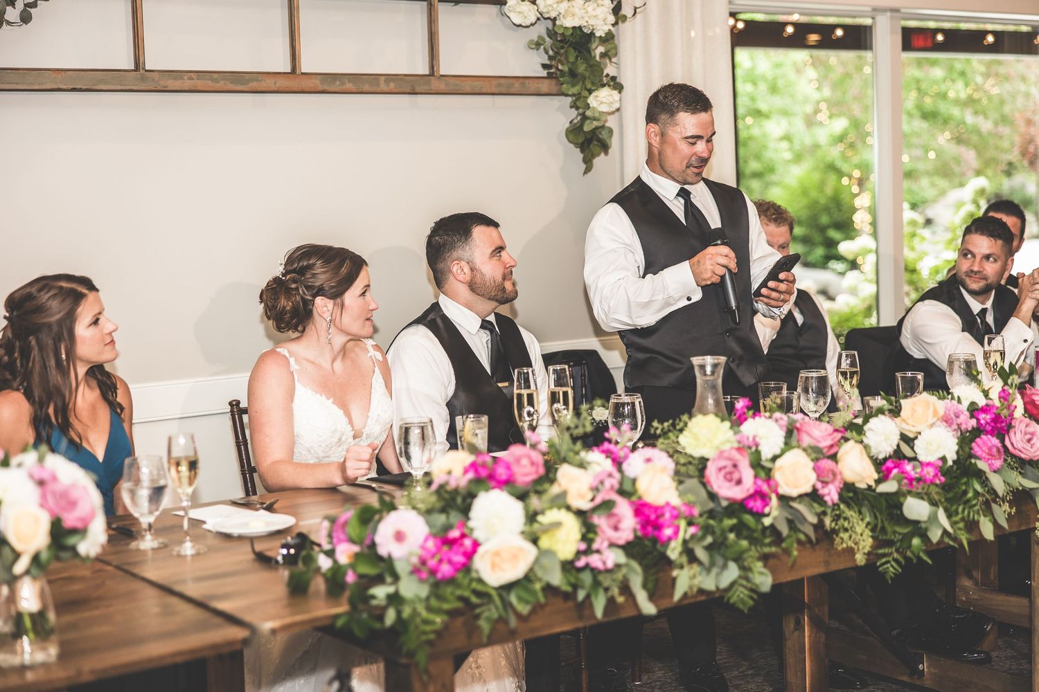 Wedding reception venue decorated with pink and white floral arrangements and rustic wooden tables.
