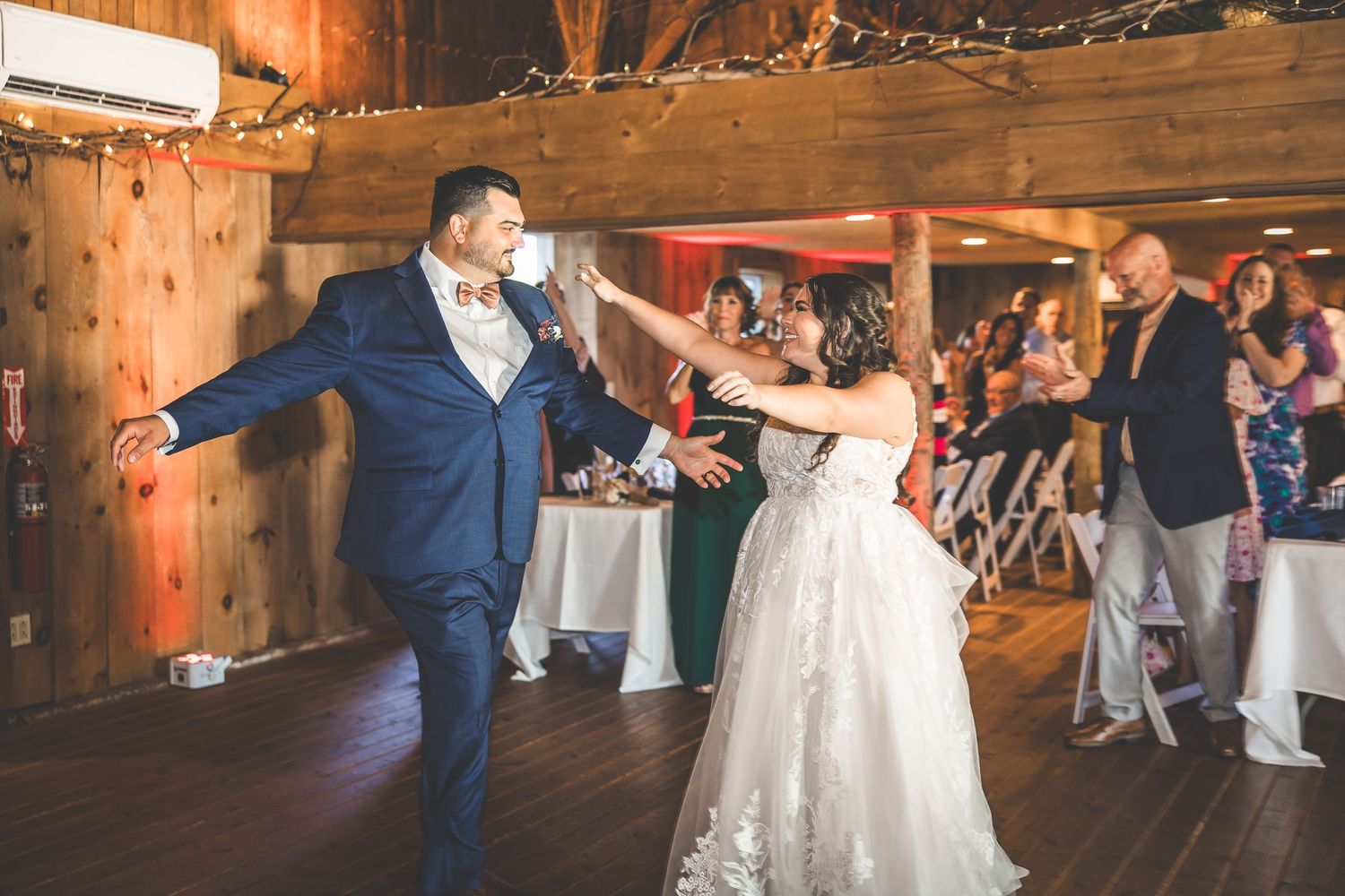 Wedding guests dancing and celebrating in rustic barn reception venue with twinkle lights.