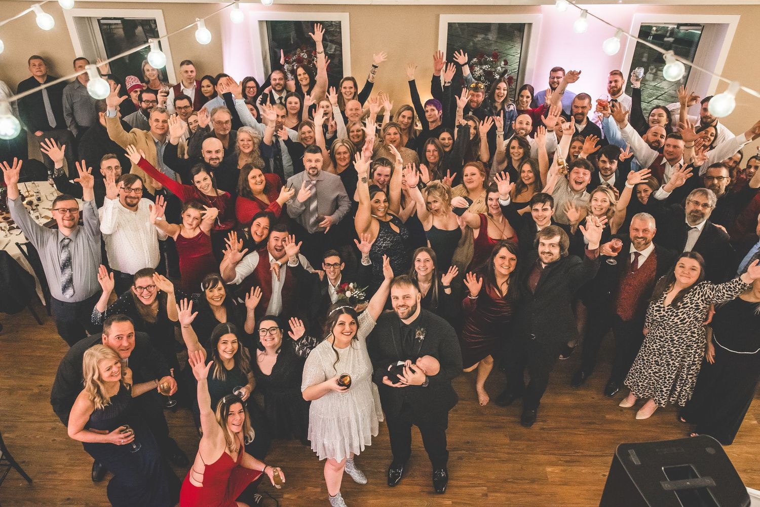 Large group of wedding guests dancing and celebrating together in a reception hall.