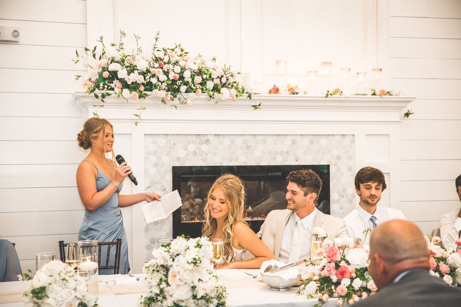 Wedding reception venue with white shiplap walls decorated with floral arrangements and elegant table settings.
