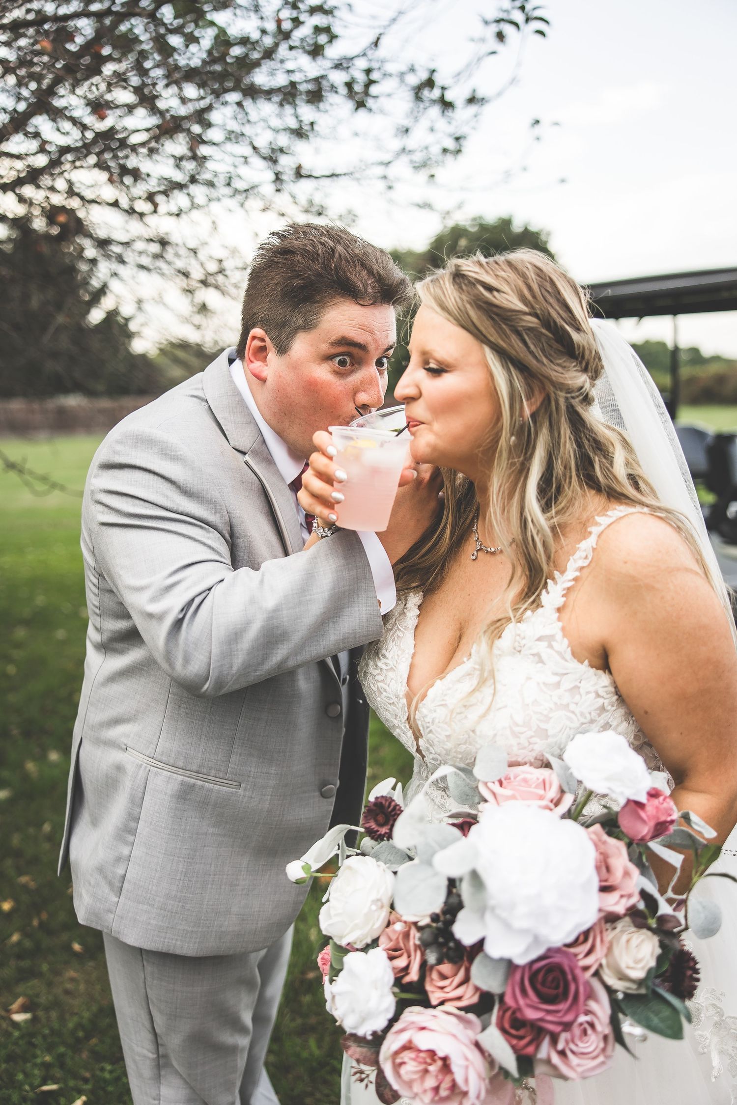 Wedding couple shares romantic moments with pink and white floral bouquet against natural backdrop.