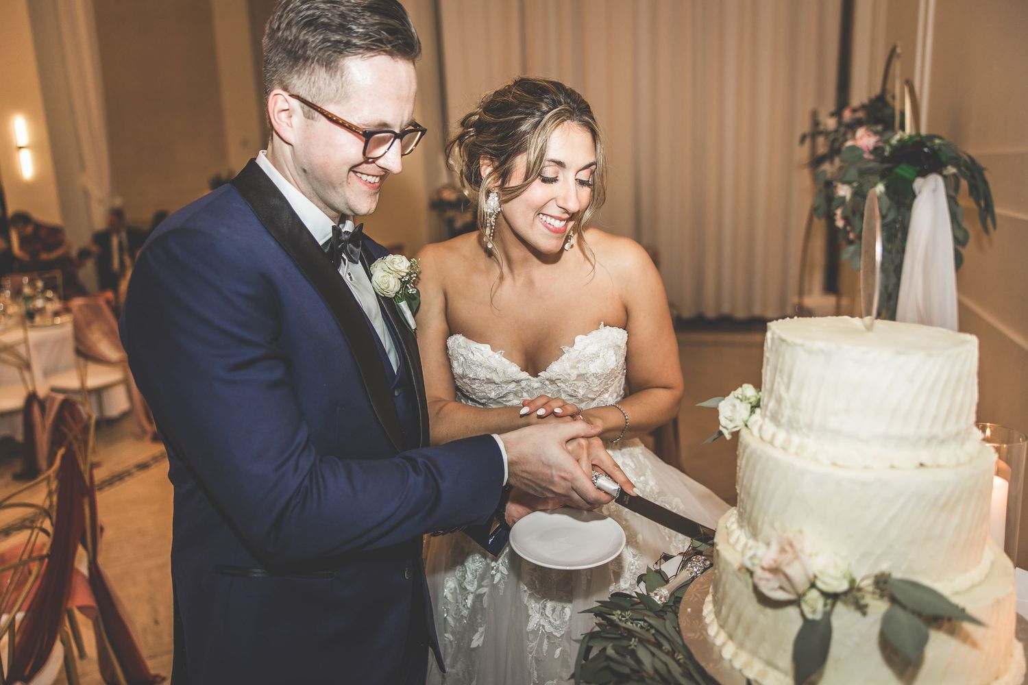 Wedding cake cutting ceremony with elegant white tiered cake at reception.
