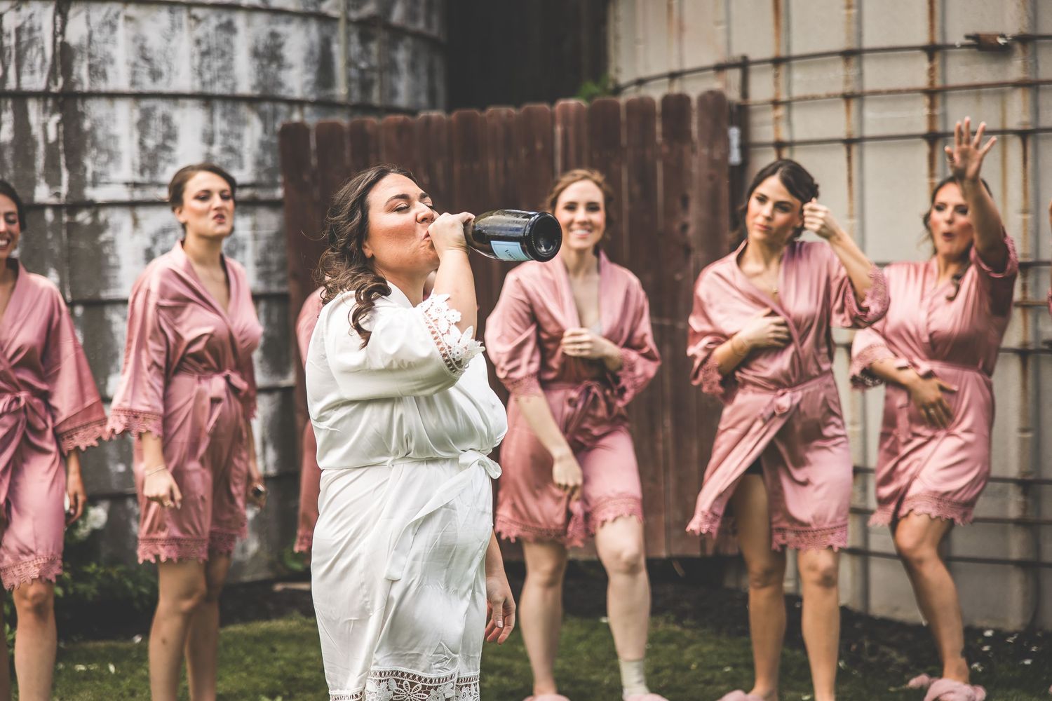 Bridal party in matching pink robes poses together against an industrial backdrop.