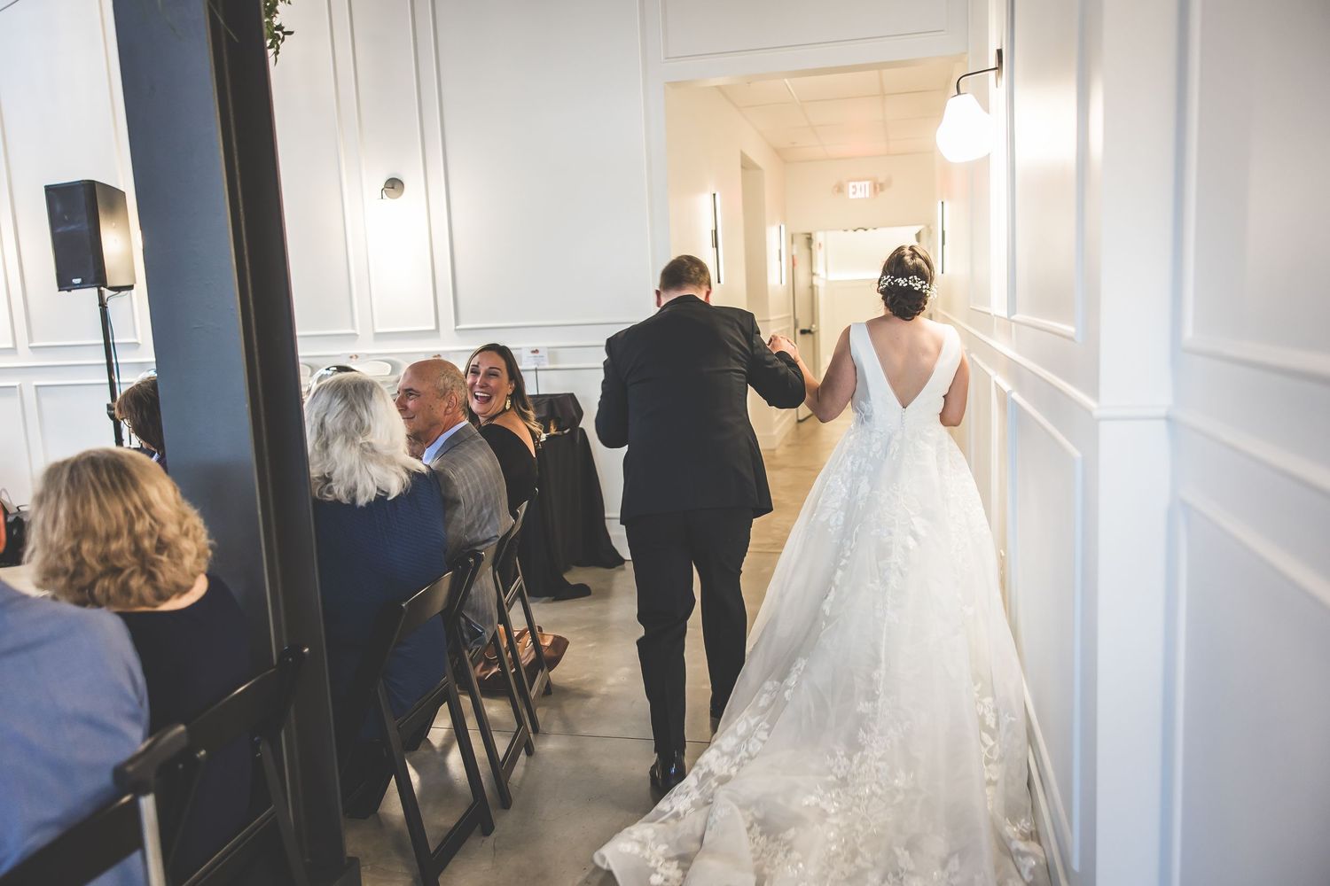 Wedding party walks down a bright hallway with white walls and modern lighting fixtures.