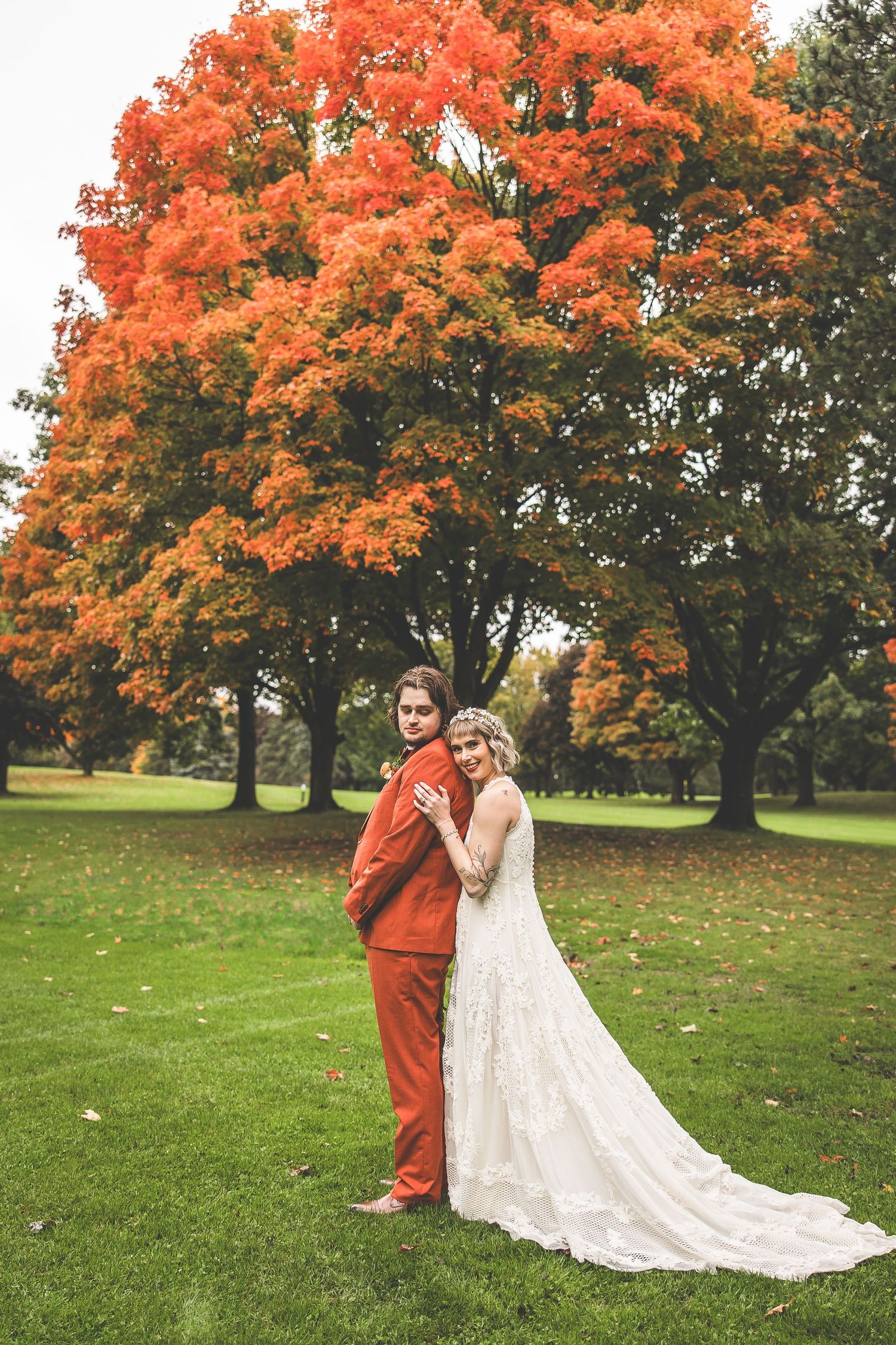 A couple shares a romantic moment under vibrant orange autumn trees on their wedding day.