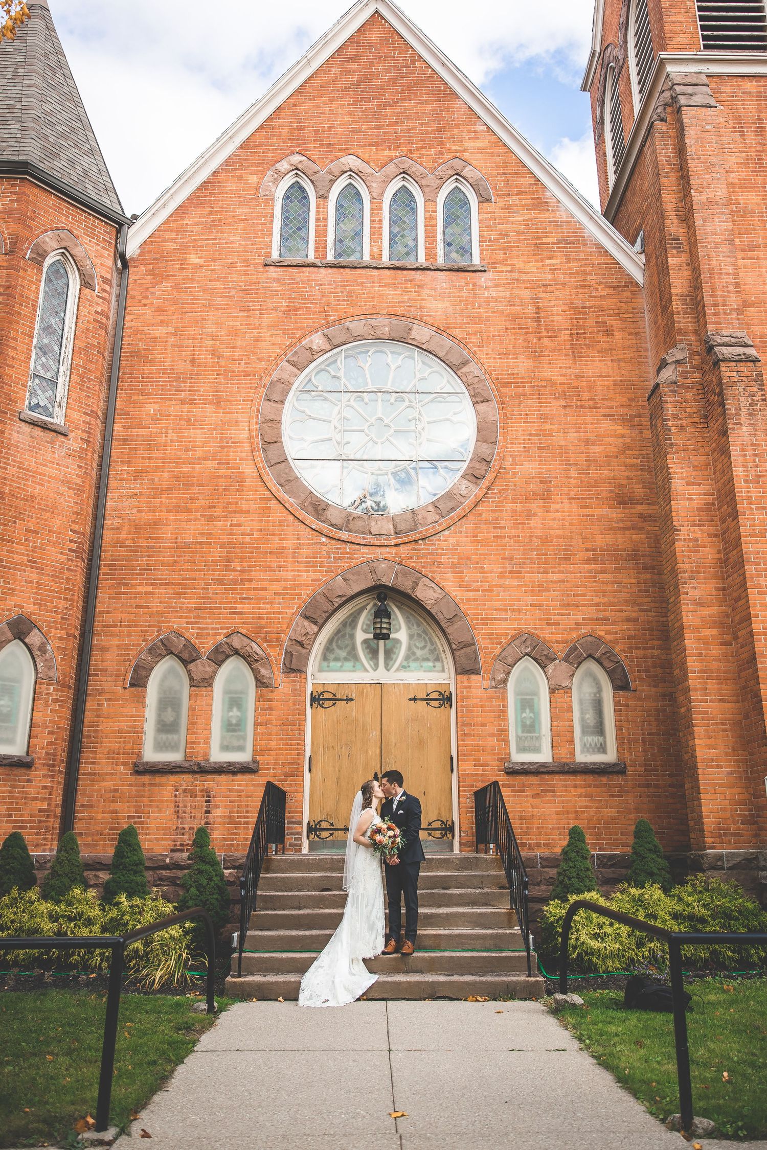 Wedding photos taken outside historic red brick church with arched windows and wooden doors.